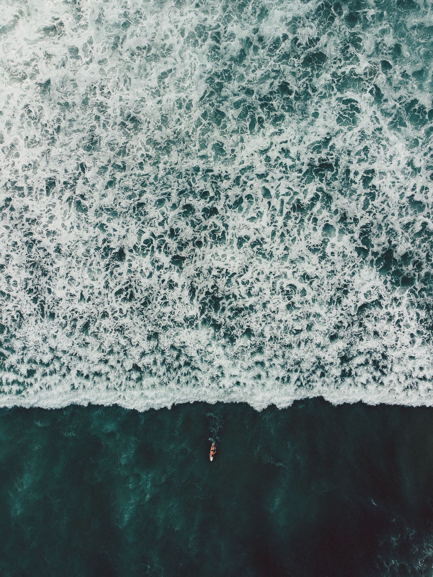 Aerial view of white ocean waves crashing against deep turquoise waters.