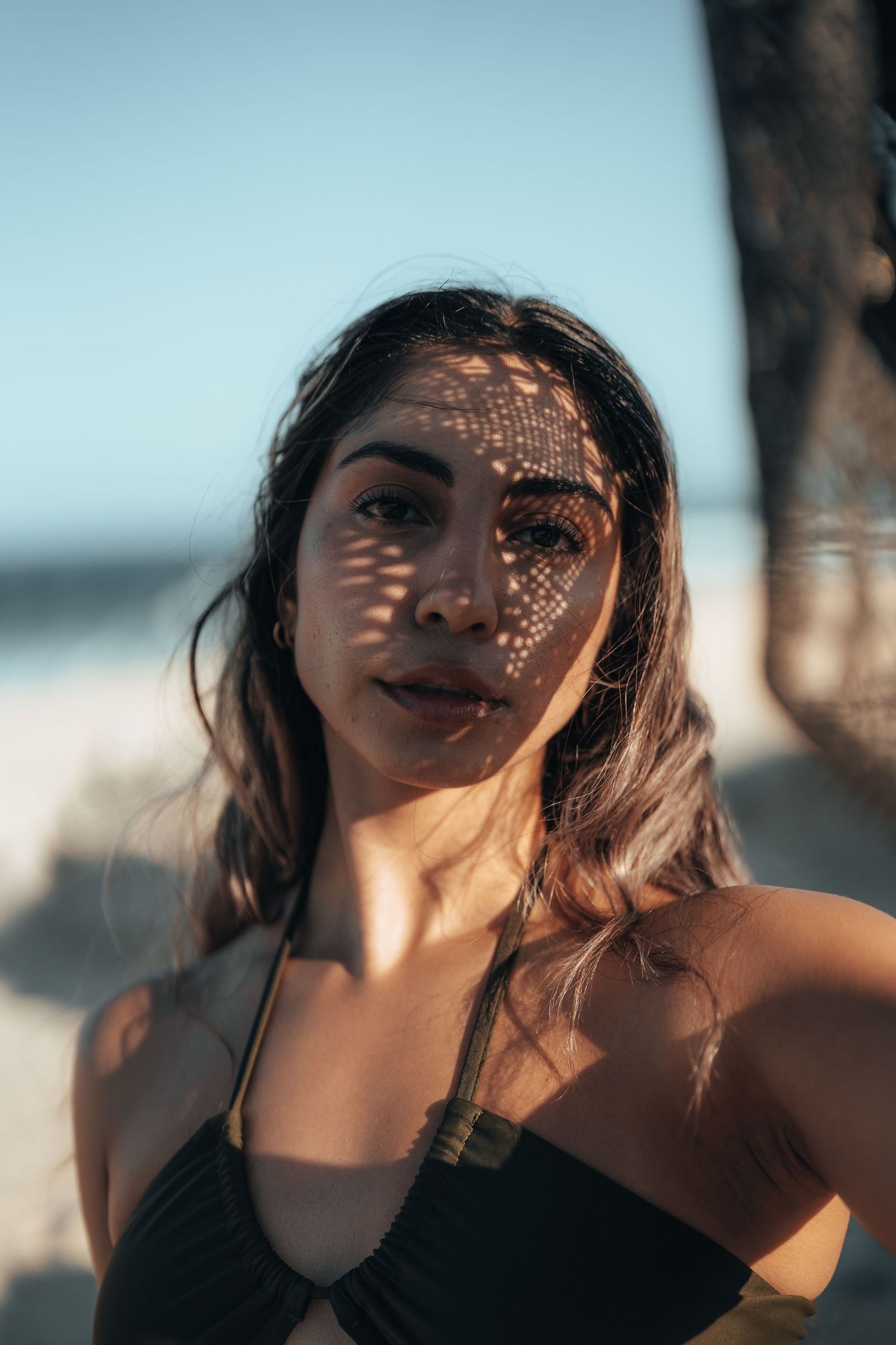 Artistic beach portrait with dappled light creating patterns on skin during golden hour.