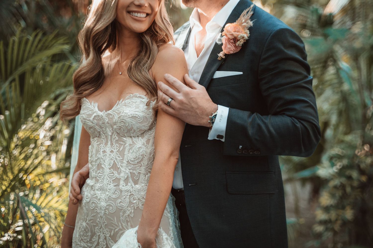 Romantic wedding couple embraces in a lush garden setting with warm sunlight filtering through greenery.