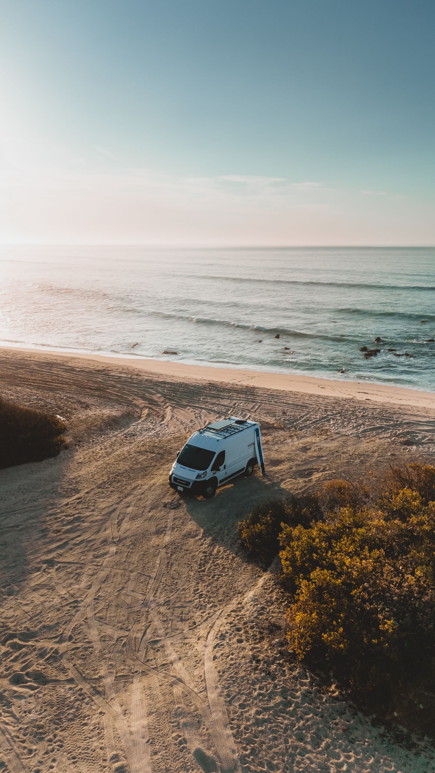 A silver SUV parked on a coastal cliff overlooking the ocean during golden hour.
