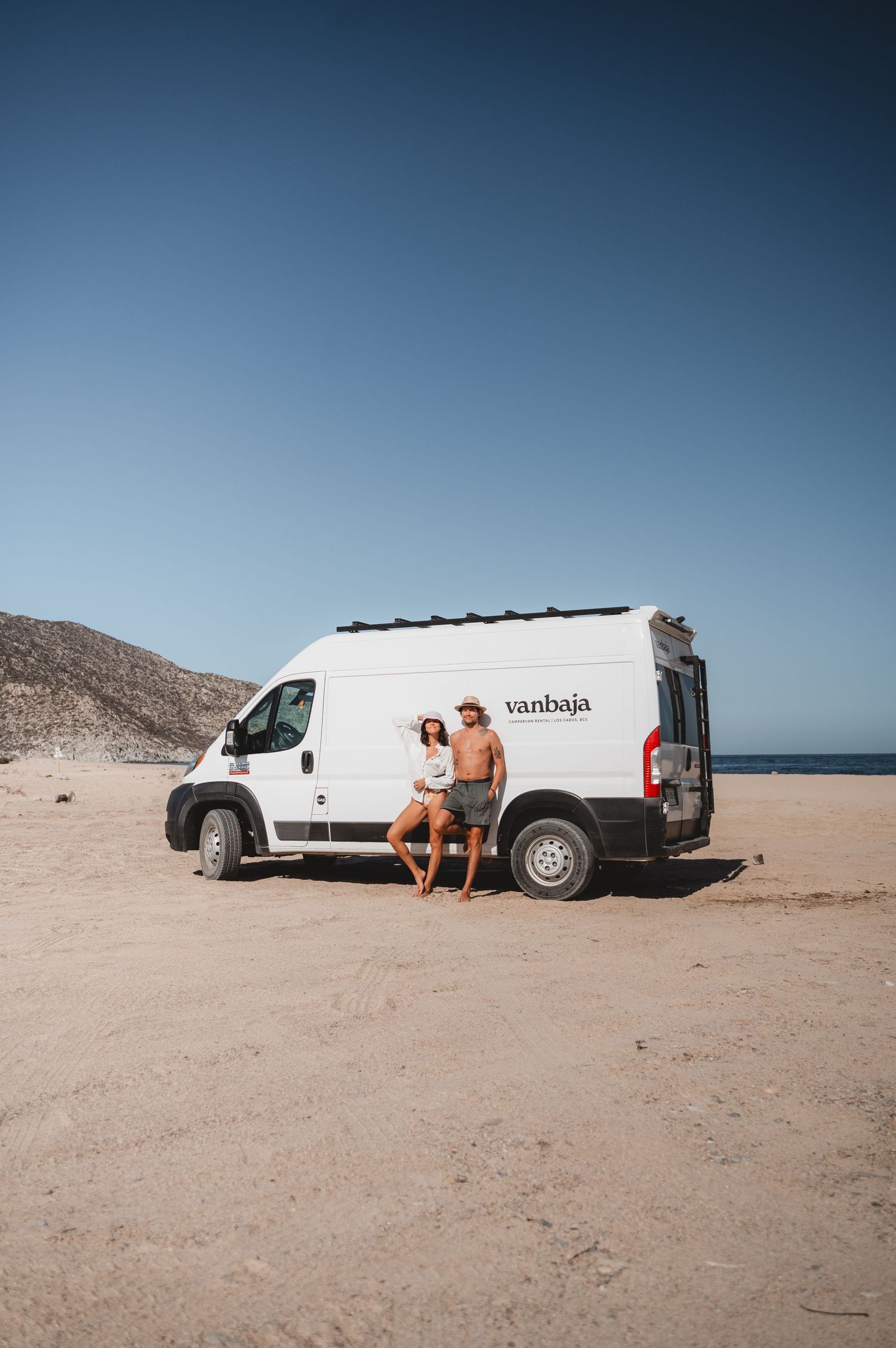 White campervan parked on desert beach with ocean view.