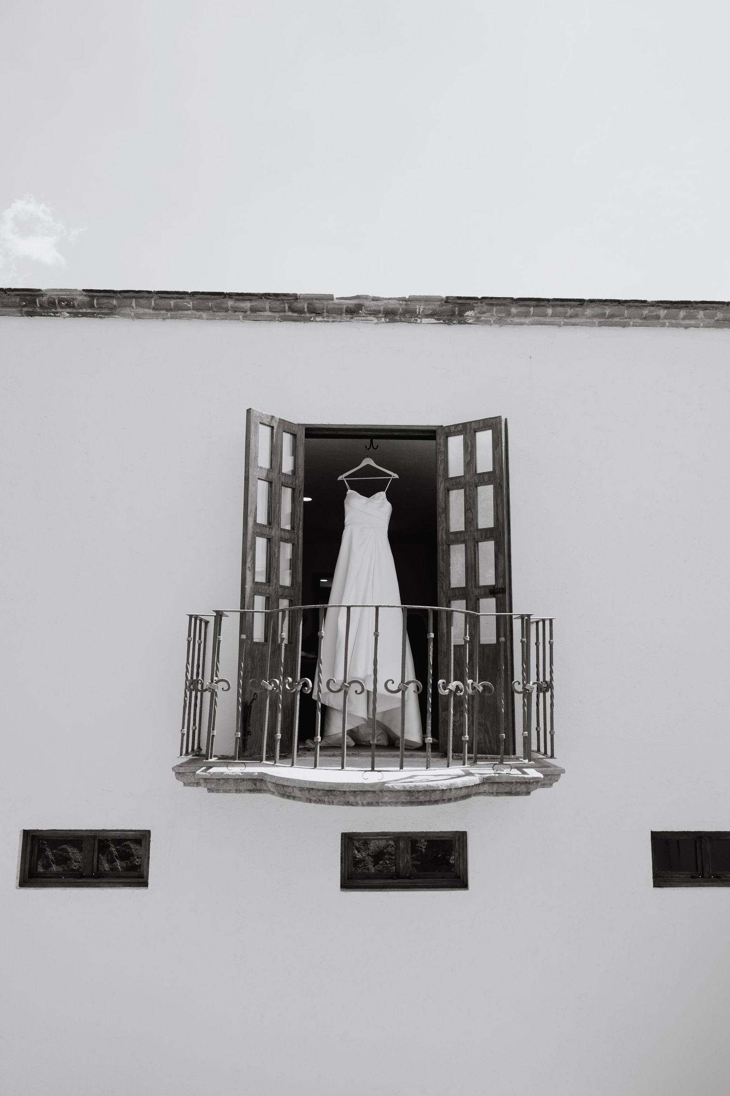 Wedding dress hanging in an open window frame against a white Mediterranean building exterior.