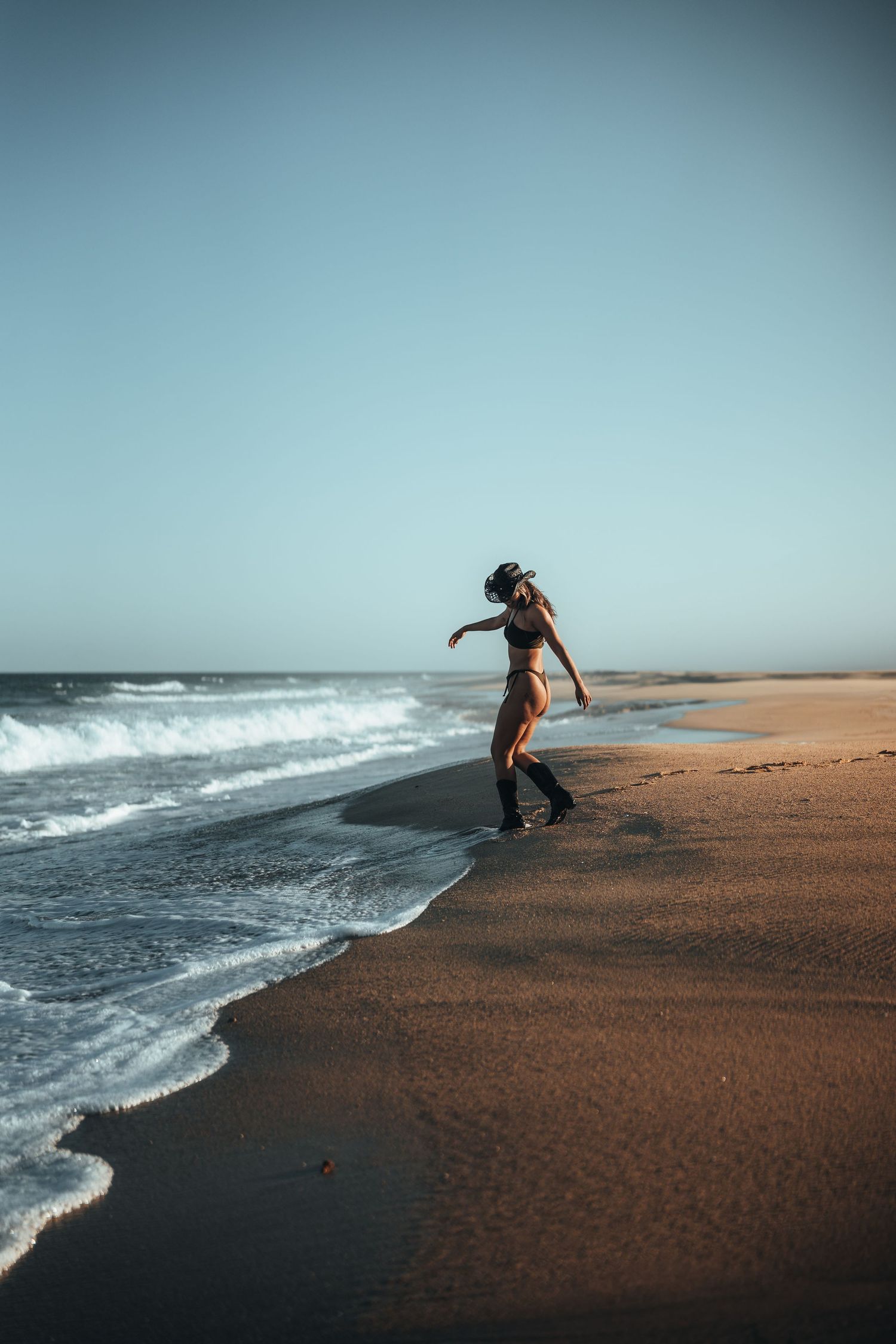 A silhouetted figure dances along the shoreline where ocean waves meet sandy beach at sunset.