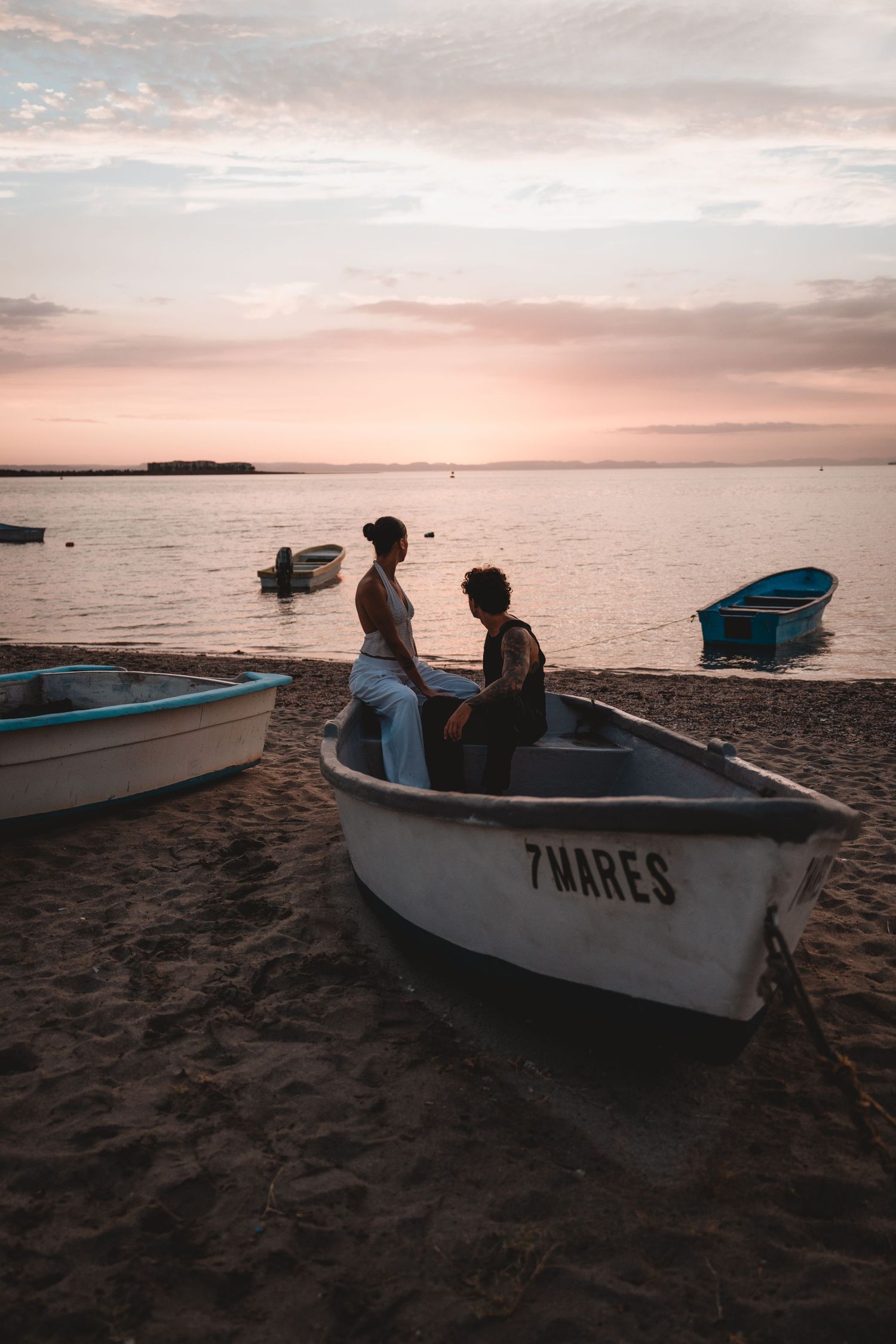 Small fishing boats labeled '7 Mares' resting on beach sand at sunset.