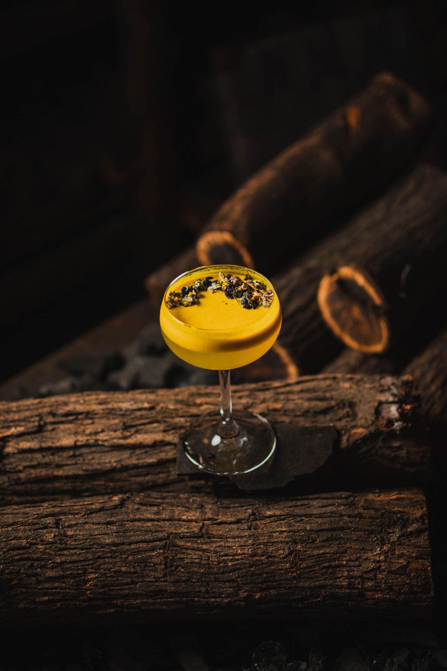 Yellow cocktail garnished with berries served on rustic wooden surface in dark lighting.