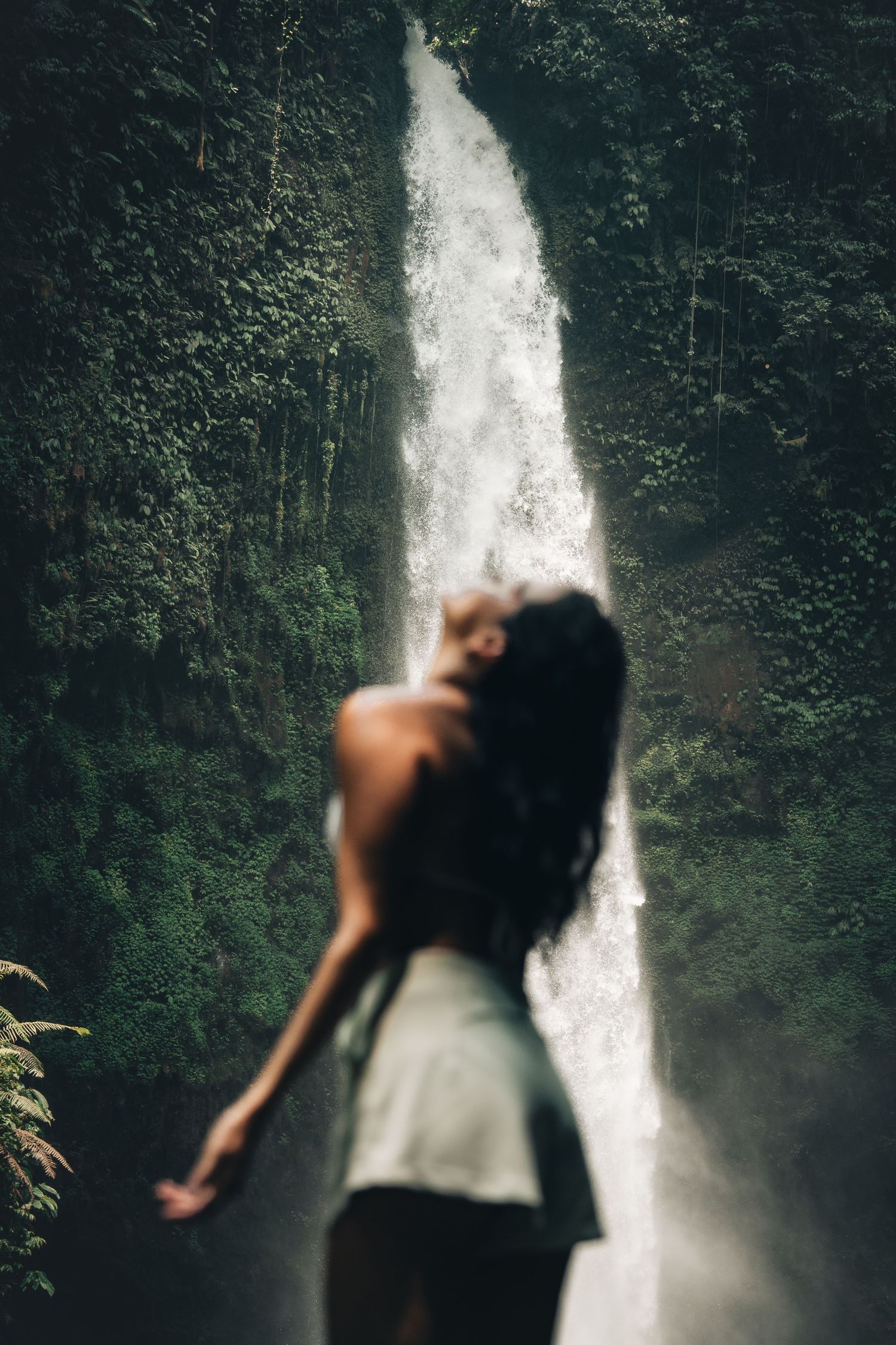 Artistic silhouette against misty waterfall backdrop in tropical forest setting.