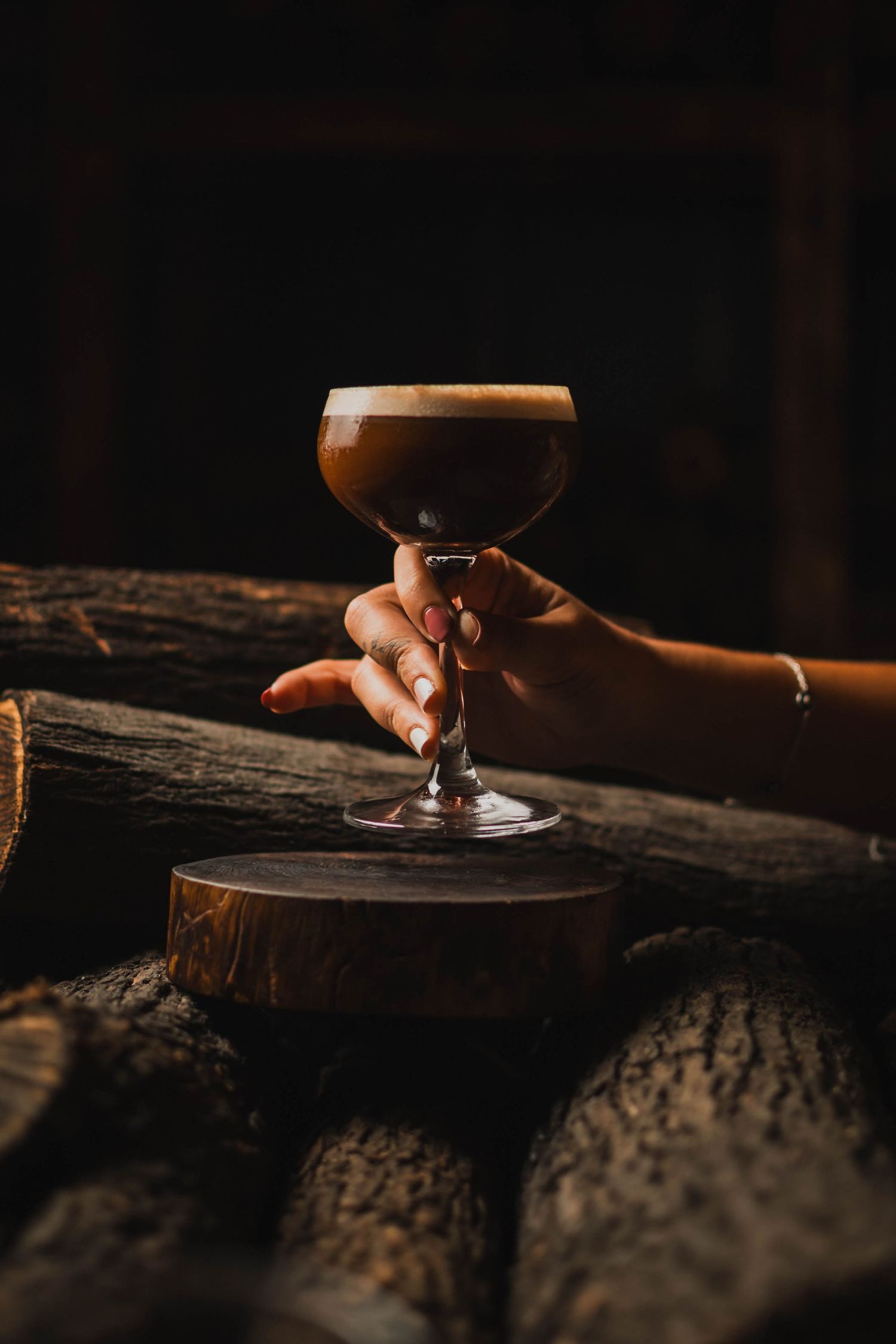 Cocktail glass held against textured wood surface in dramatic low-key lighting.
