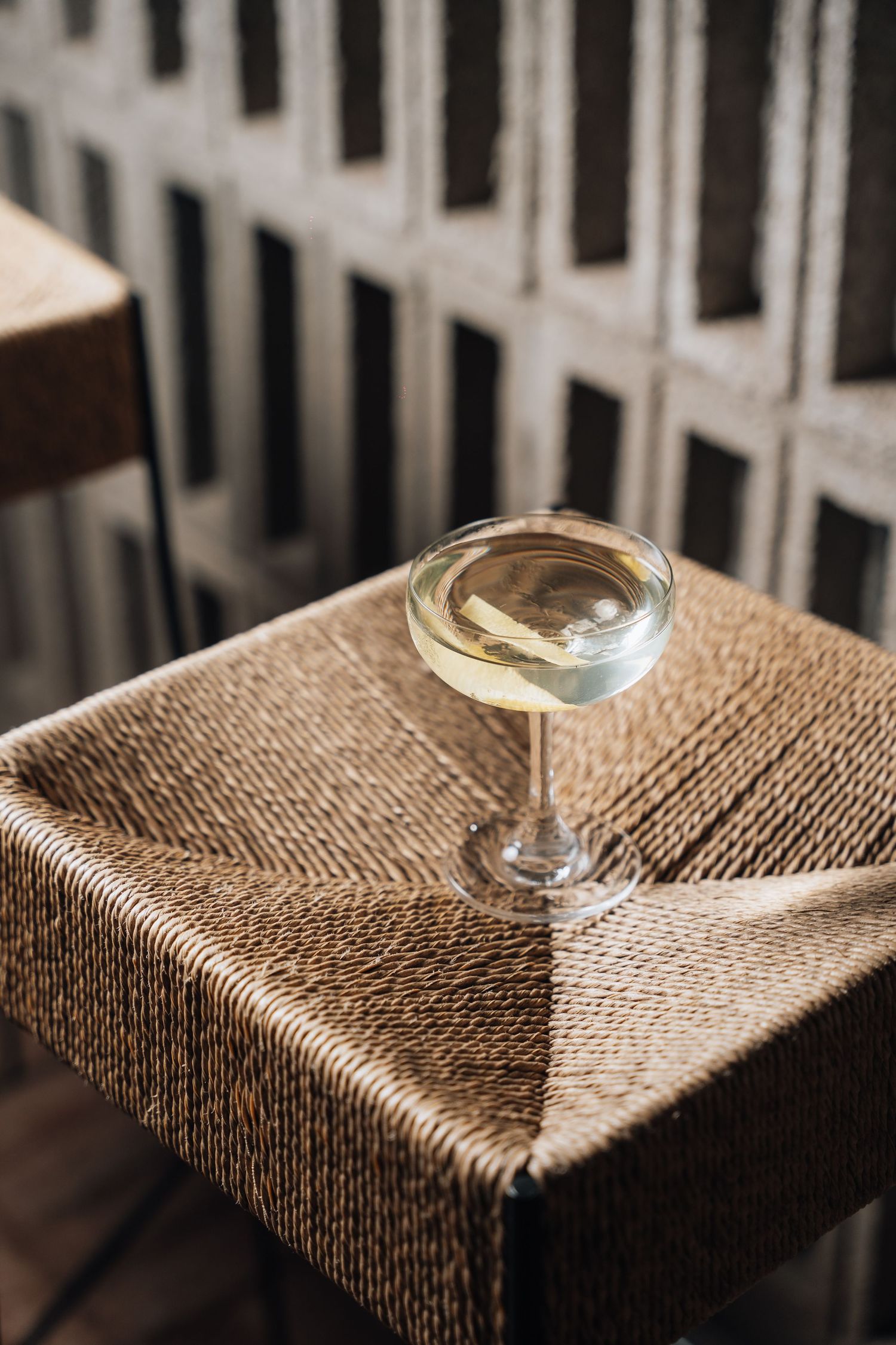 Martini glass with clear cocktail sitting on textured woven surface in moody lighting.