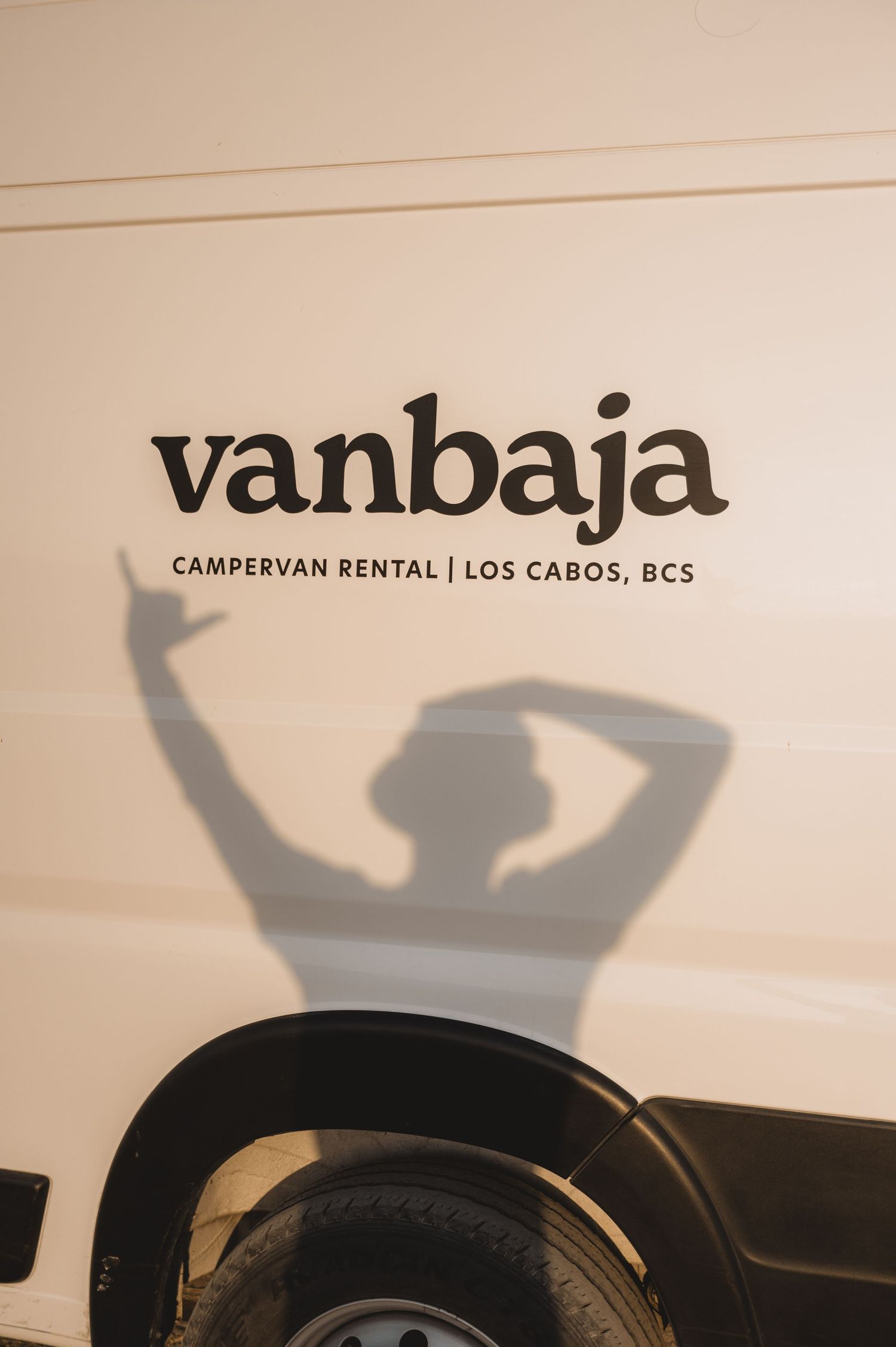 Shadow silhouettes against wall displaying Vanbaja campervan rental text.