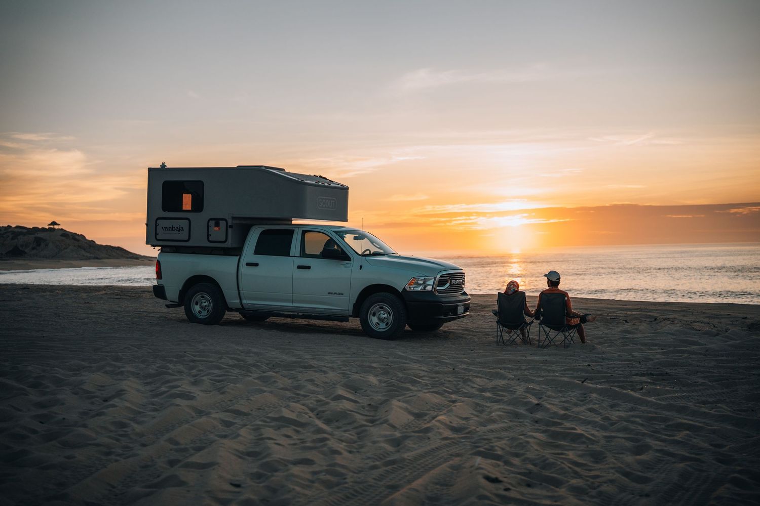 Silhouetted vehicles and people on a beach during golden sunset.
