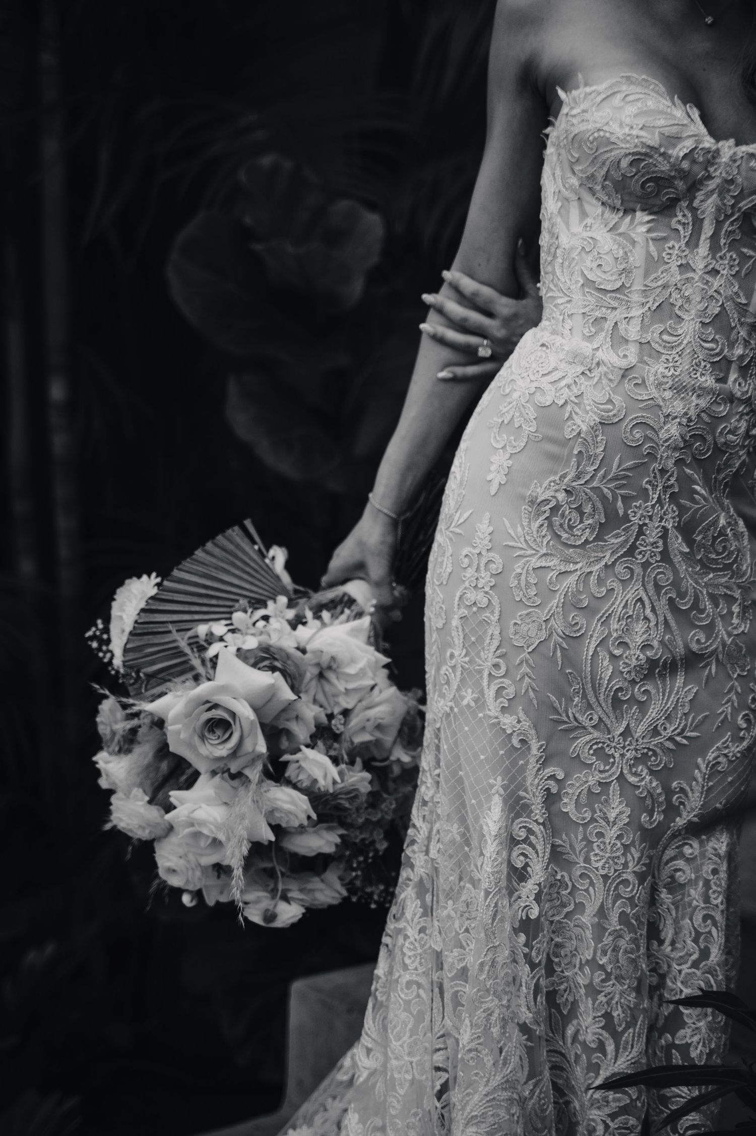 Close-up details of an intricate lace wedding dress and floral bouquet in black and white.