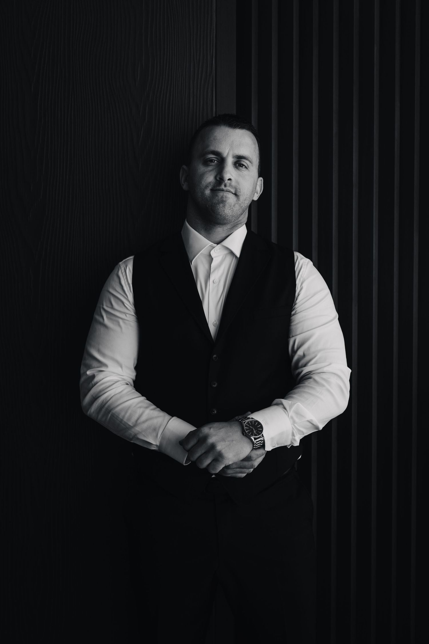 Black and white portrait of a man in formal vest and white shirt against a dark backdrop.