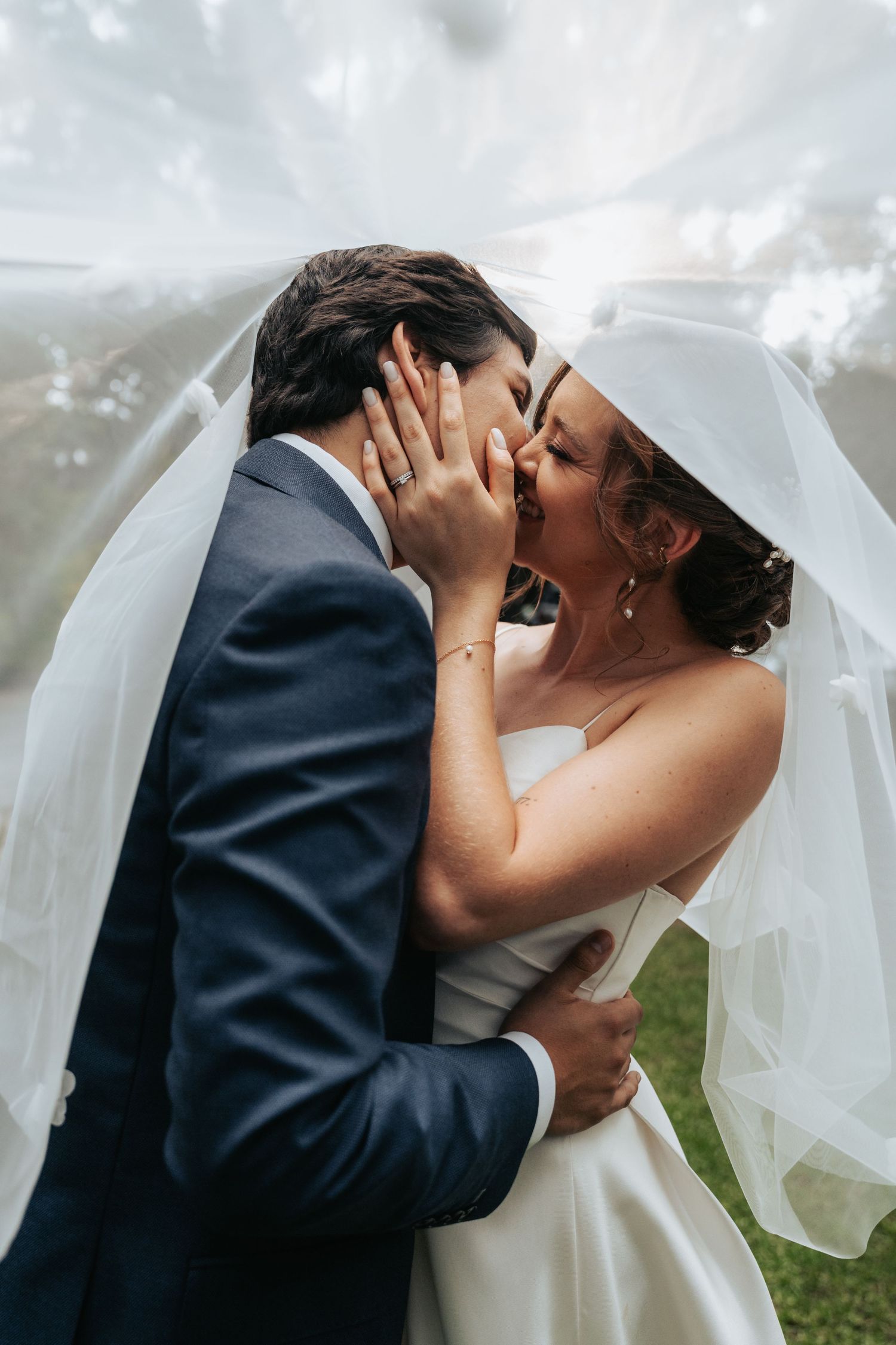 Intimate wedding kiss captured in garden setting with flowing white veil.