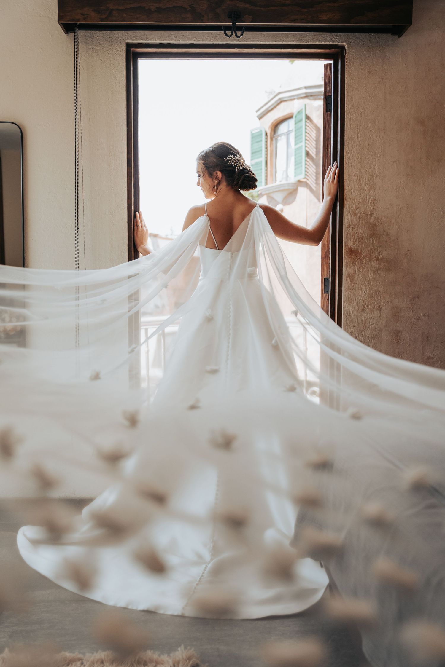 White wedding dress flowing dramatically in a sun-lit room with large windows.