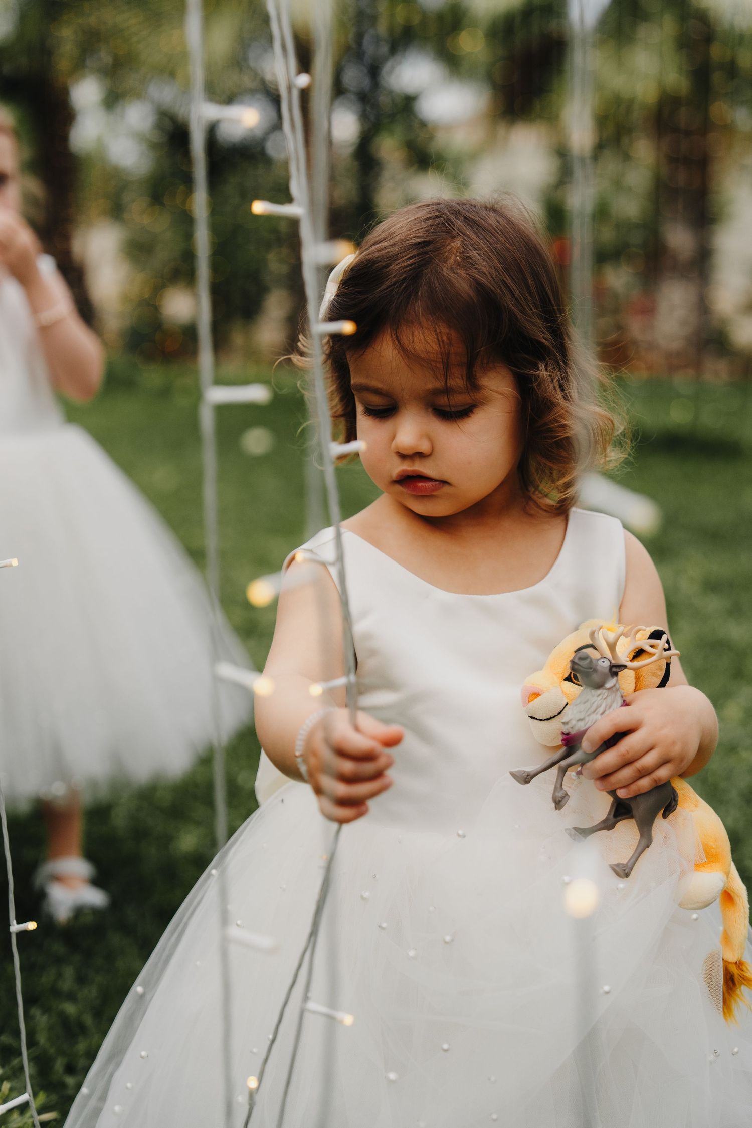Young child in white dress playing with toys during wedding celebration.