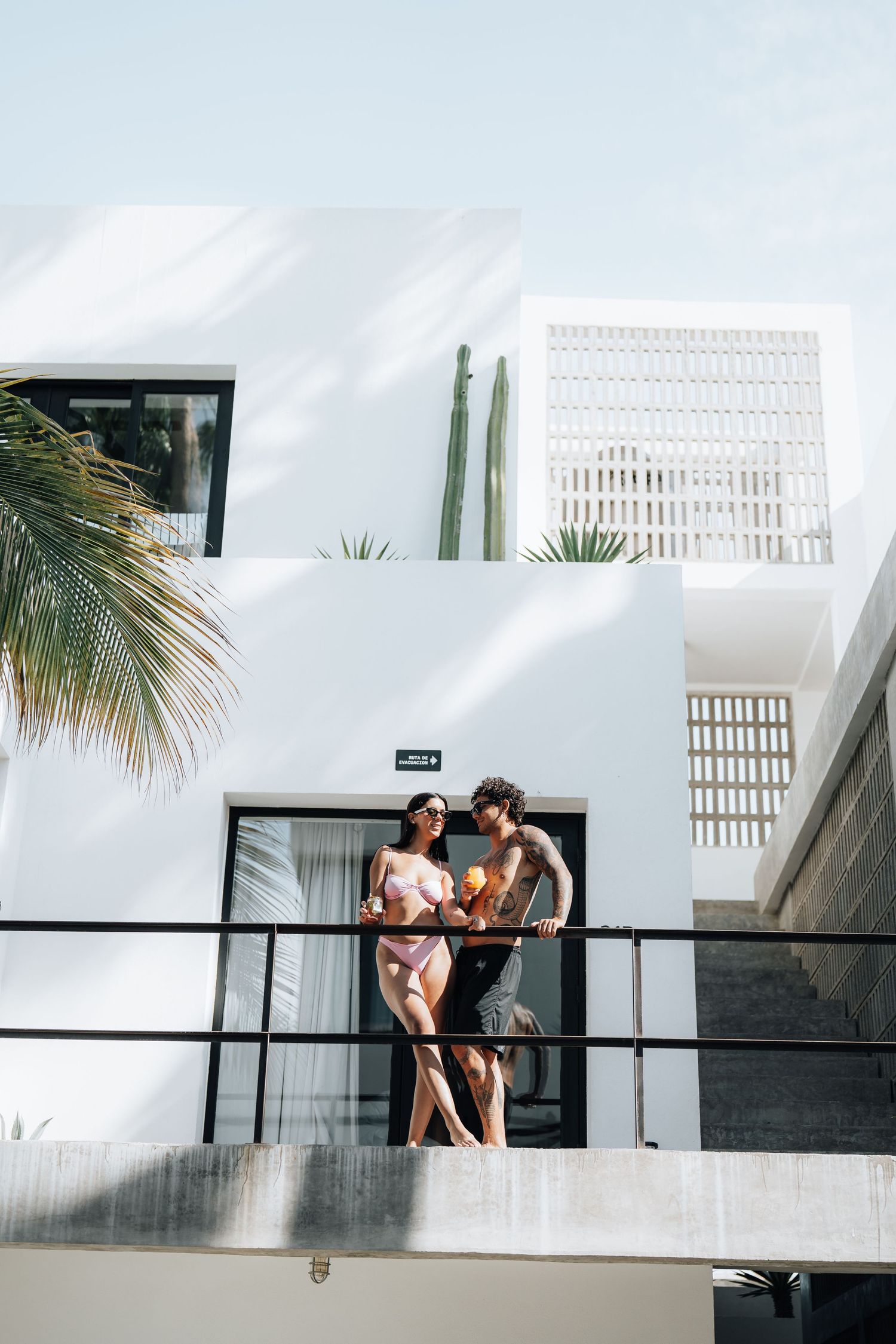 Modern white building with tropical palm trees and balcony in bright sunlight.