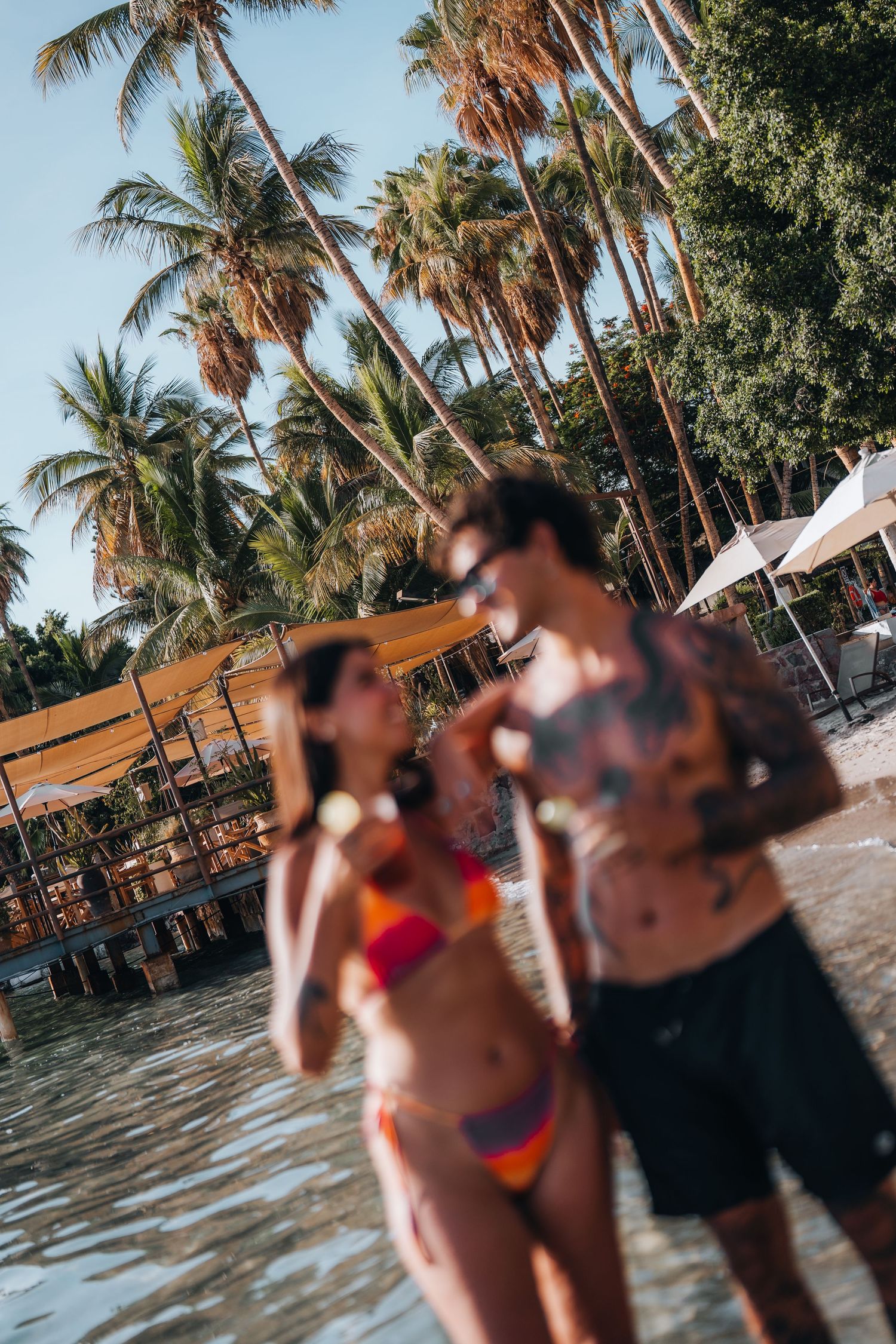 Beach scene with palm trees and people enjoying the shallow waters.