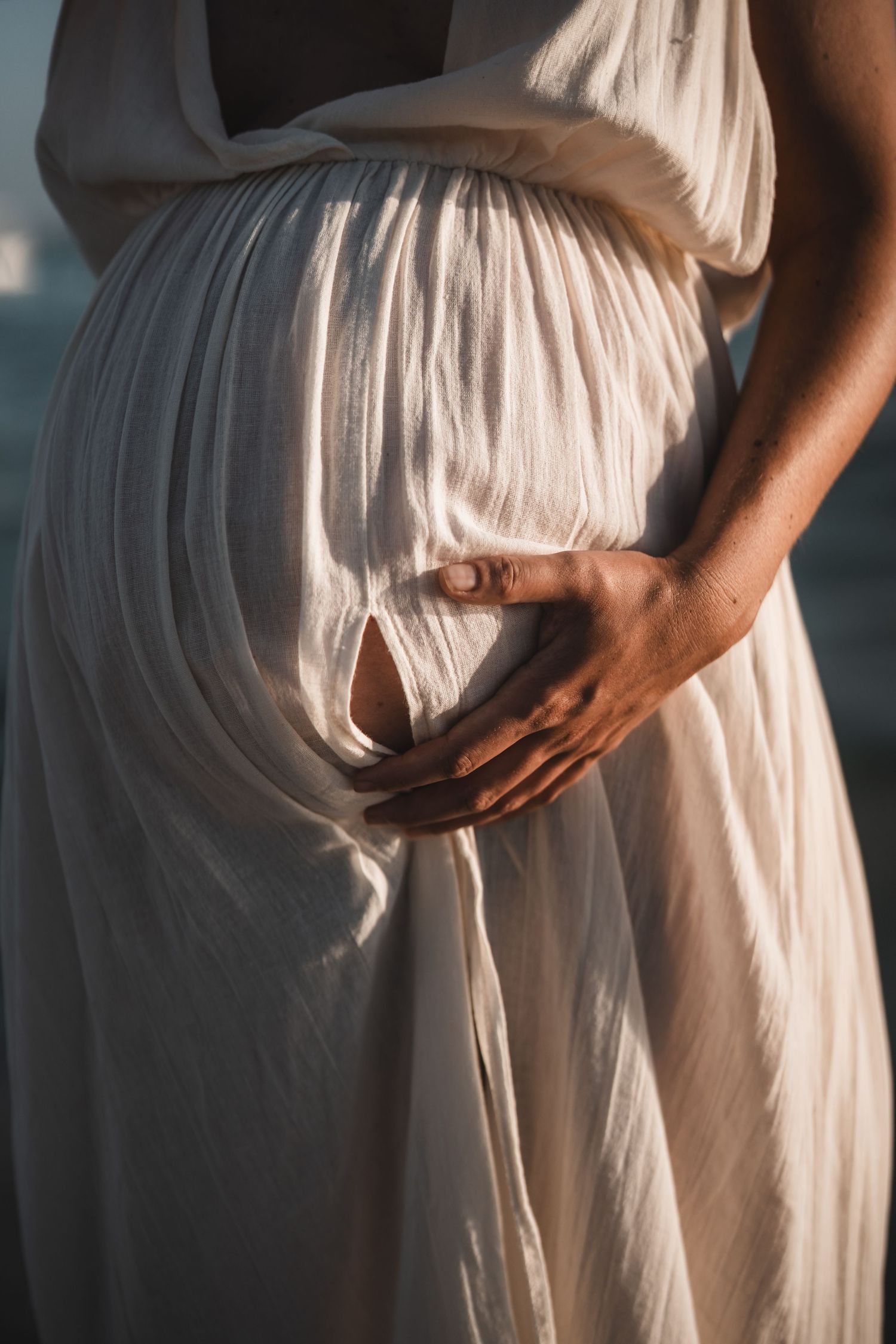 Dramatic side view of white maternity dress silhouetted against dusky water.