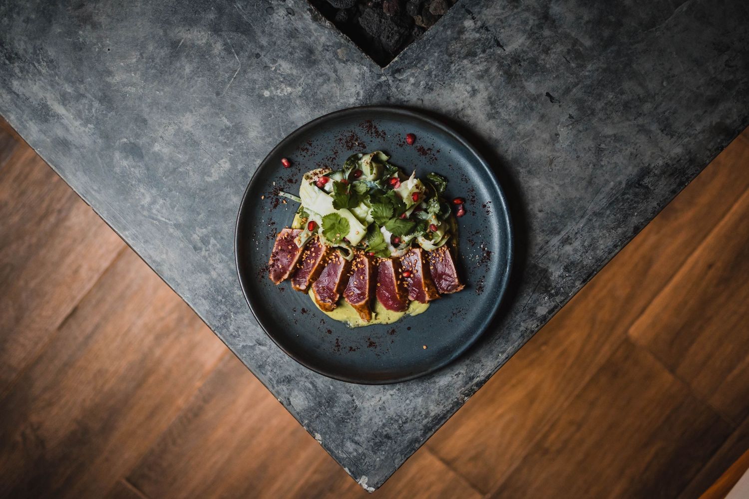 Gourmet dishes presented on dark plates against a textured grey and wooden surface.