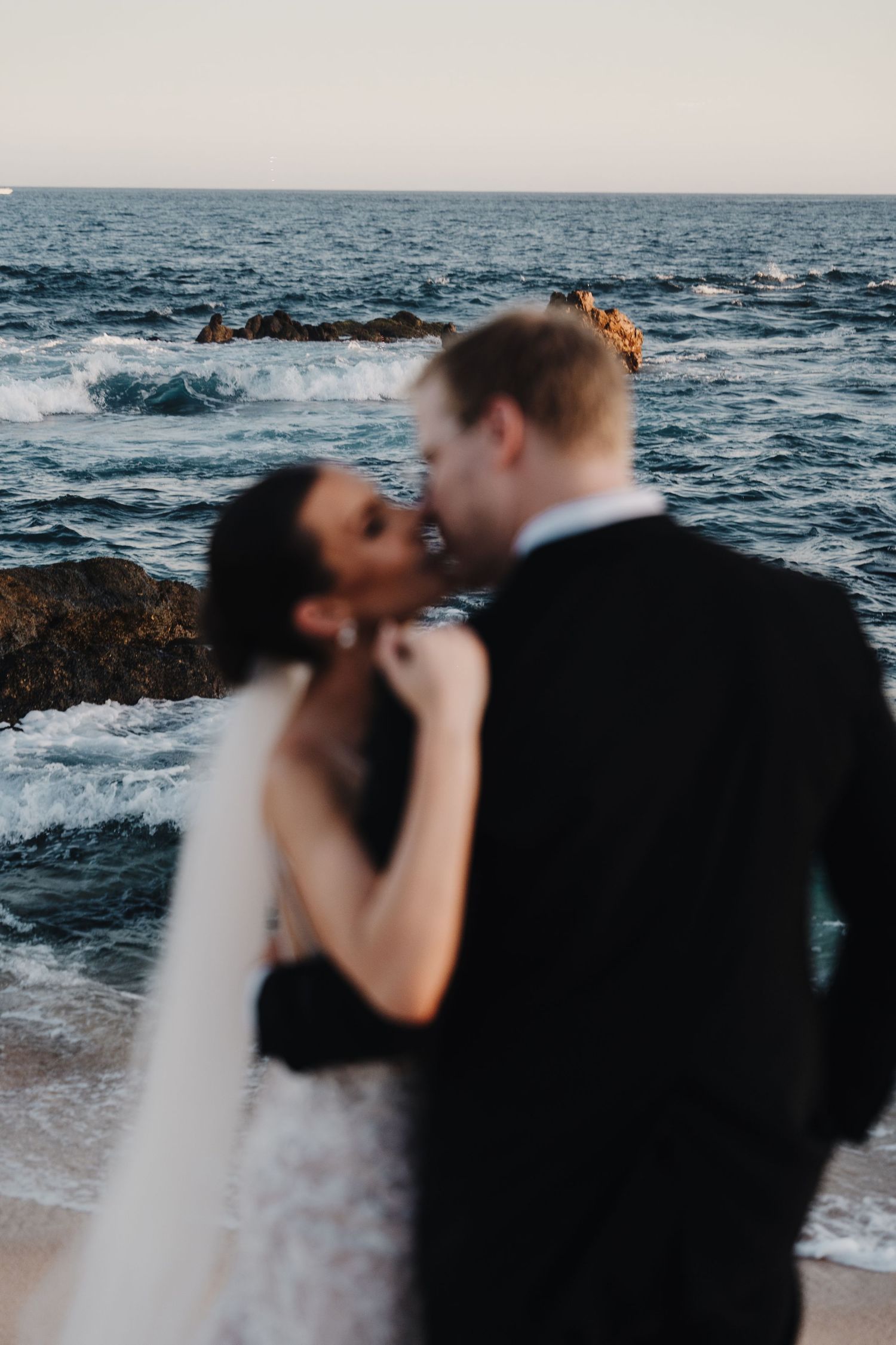 Silhouetted couple embracing on beach at dusk with ocean waves.