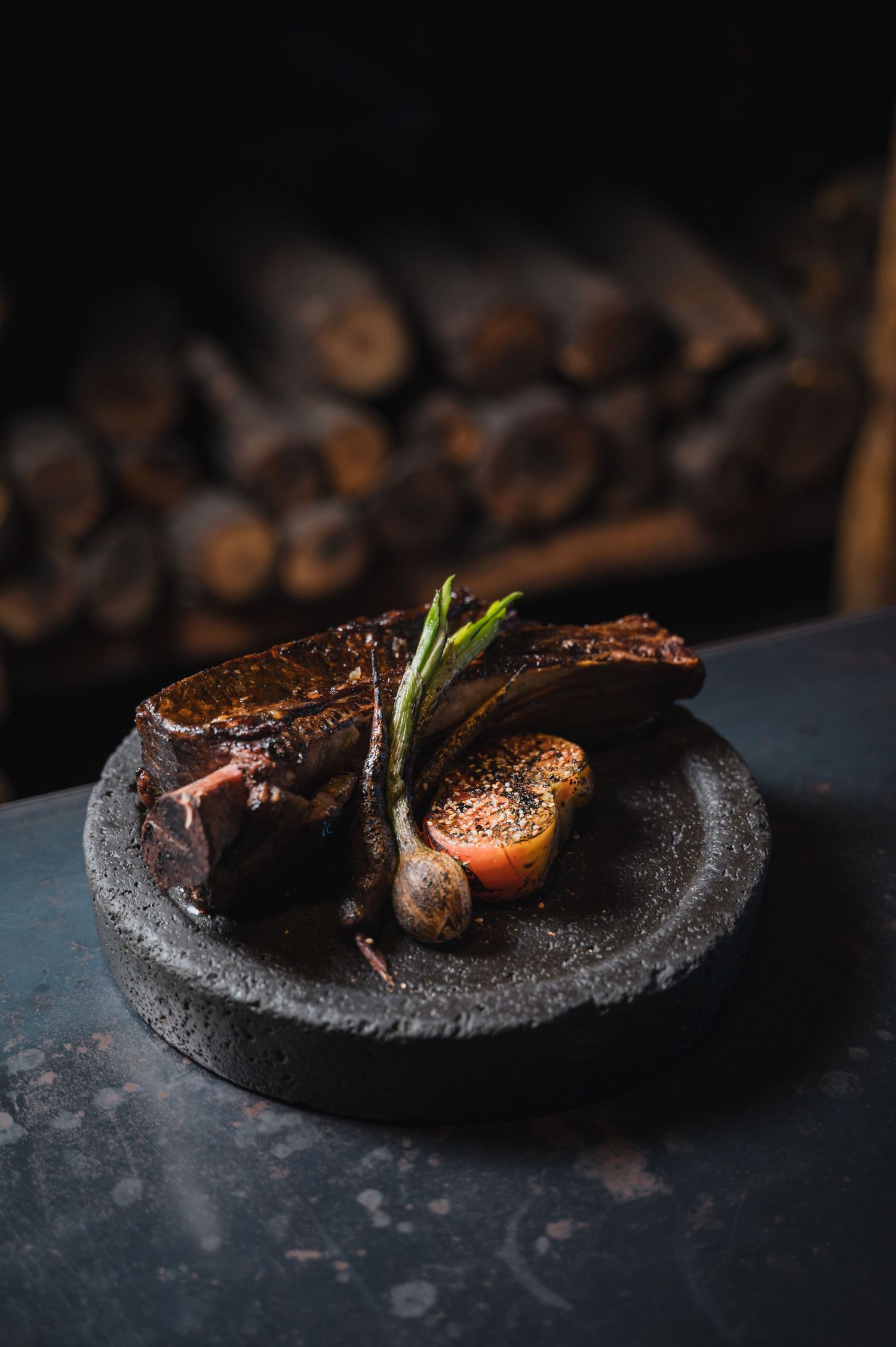 Grilled meat dish presented on a dark stone plate with garnish.