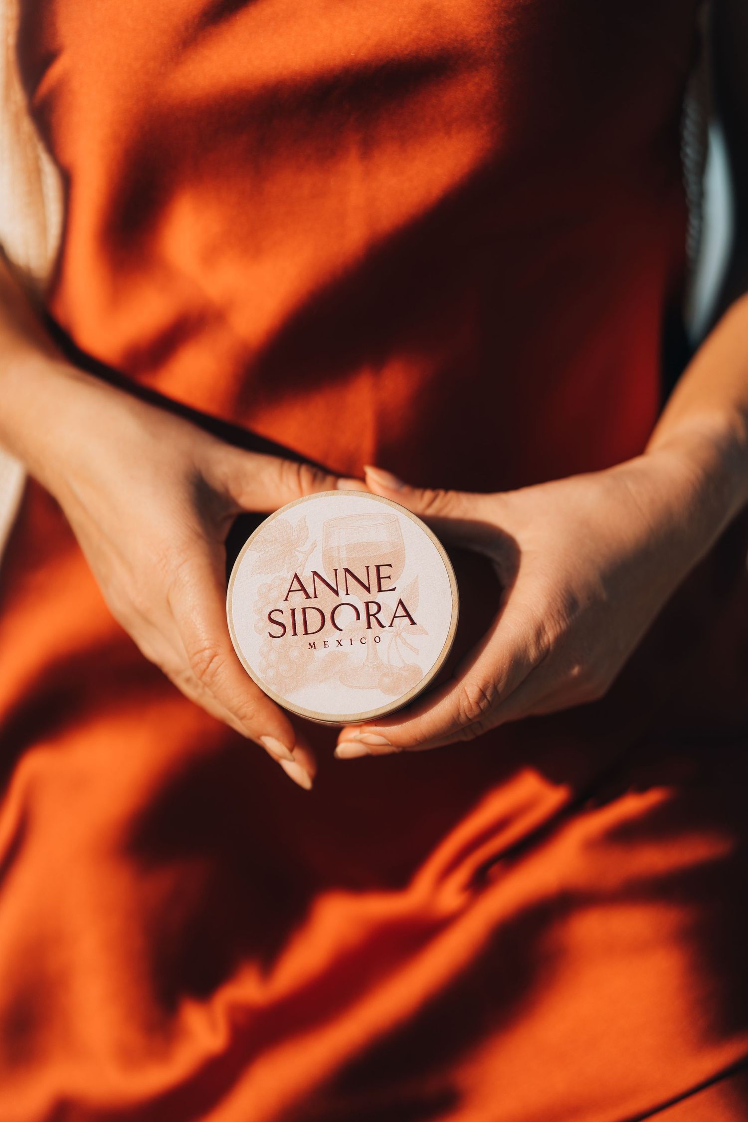 Close-up shot of hands holding 'Anne Sidora' branded product against orange background.