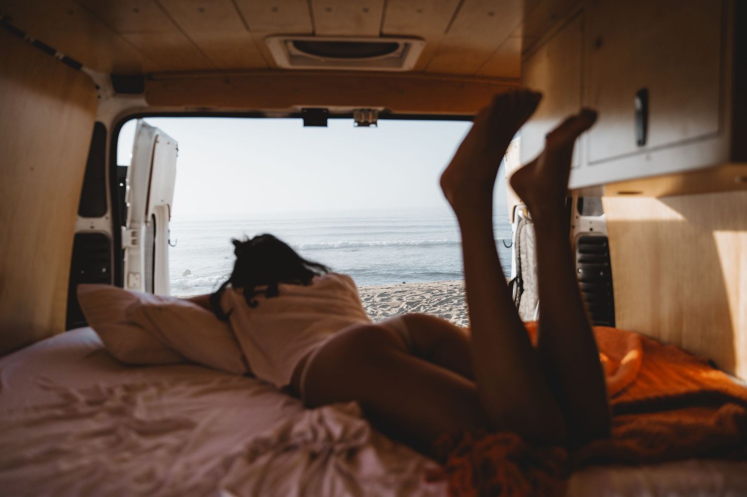 Interior view of a camper van with warm lighting and ocean views through the windows.