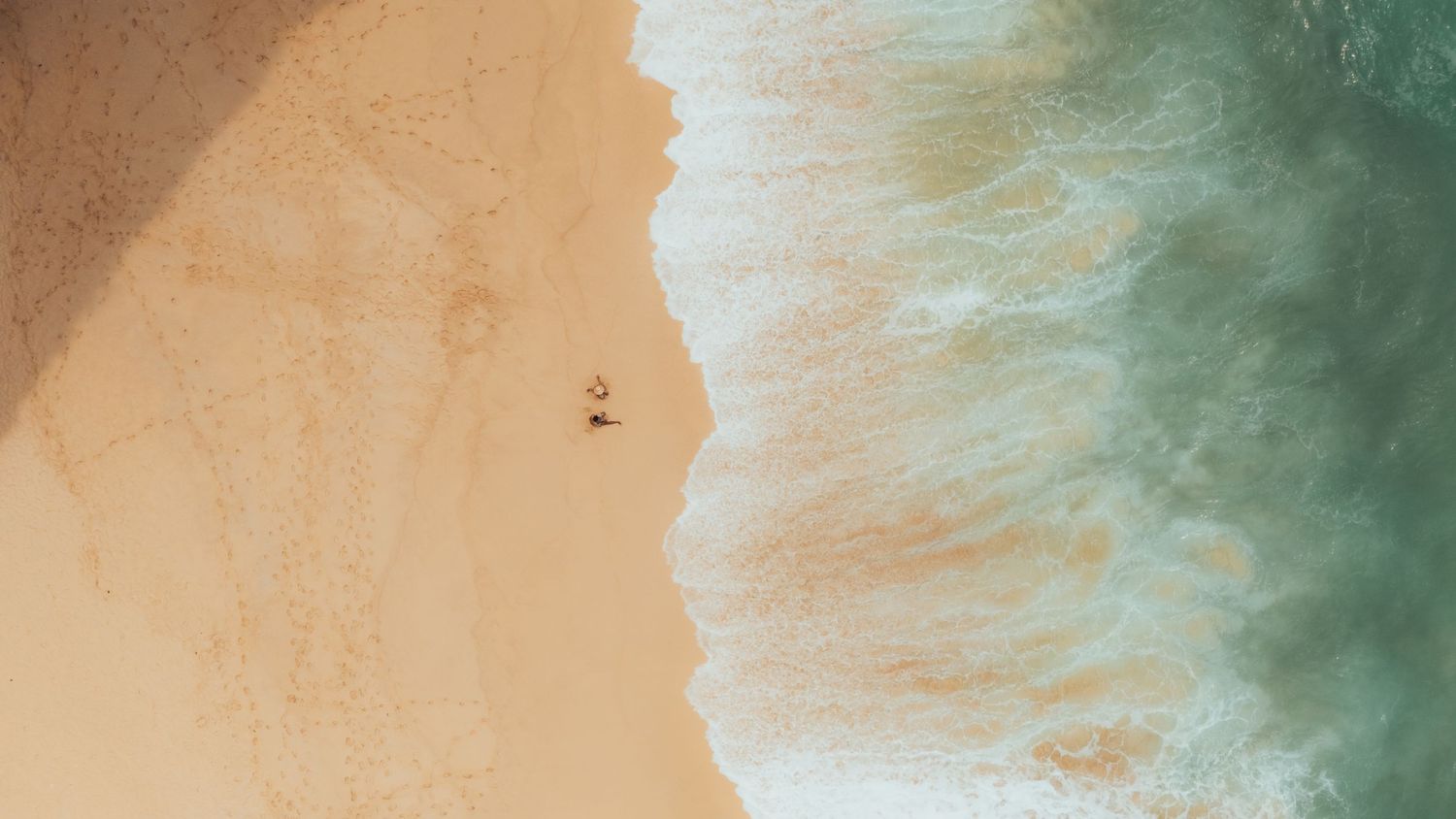 Abstract landscape view of sandy beach meeting turquoise waters from above.
