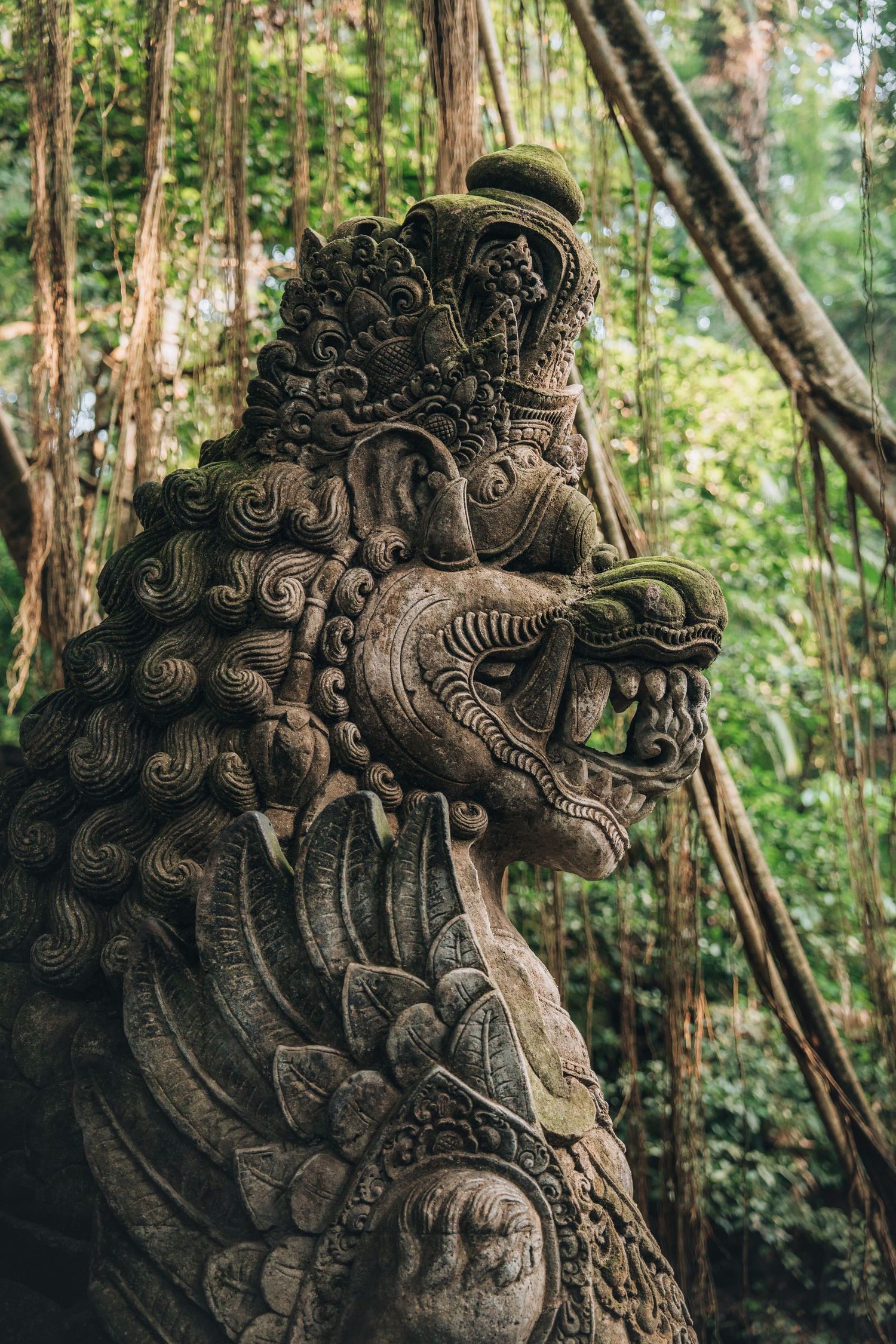 Ancient stone carved dragon statue covered in moss within tropical forest.