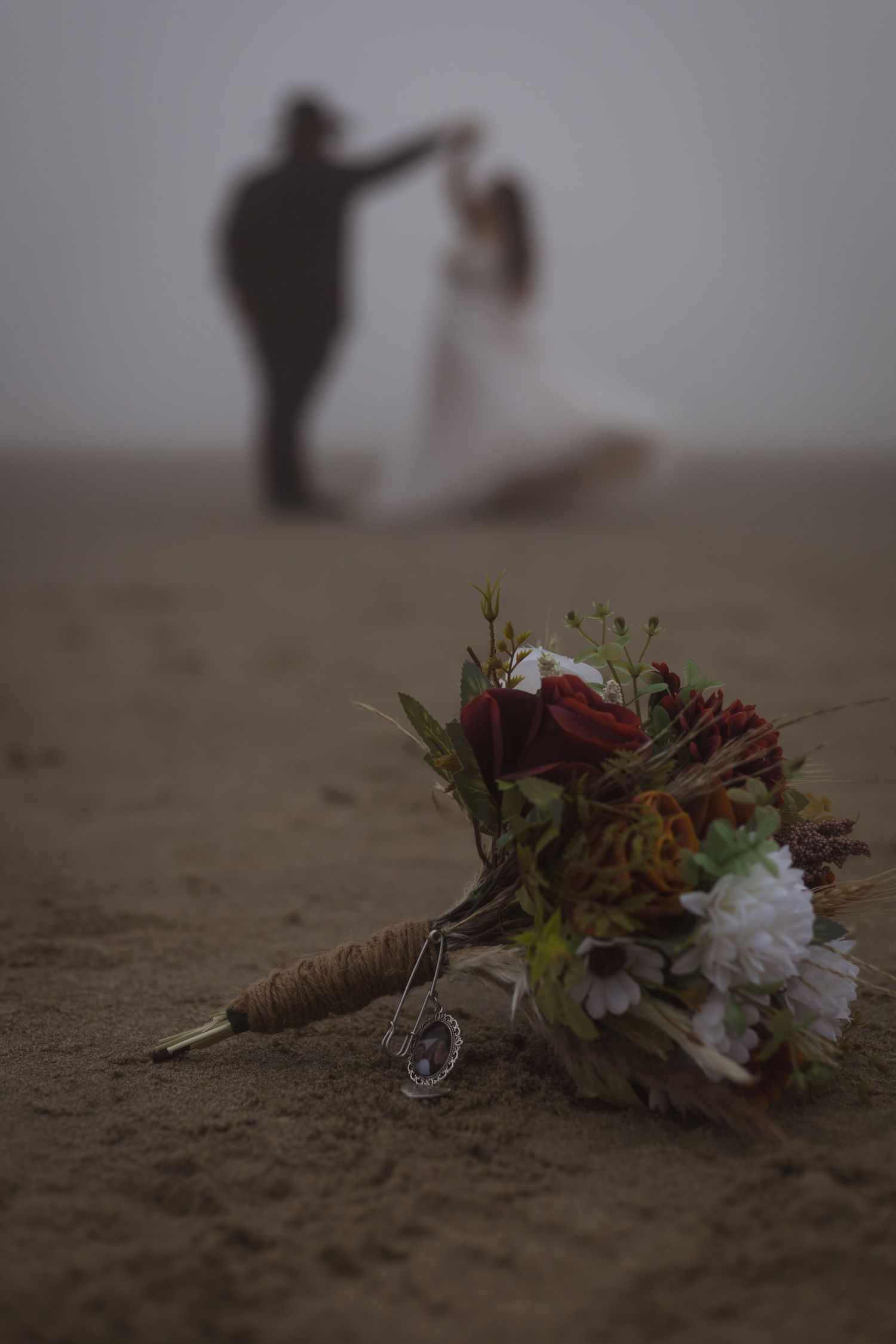 Wedding bouquet with white and burgundy flowers lying on sandy beach.
