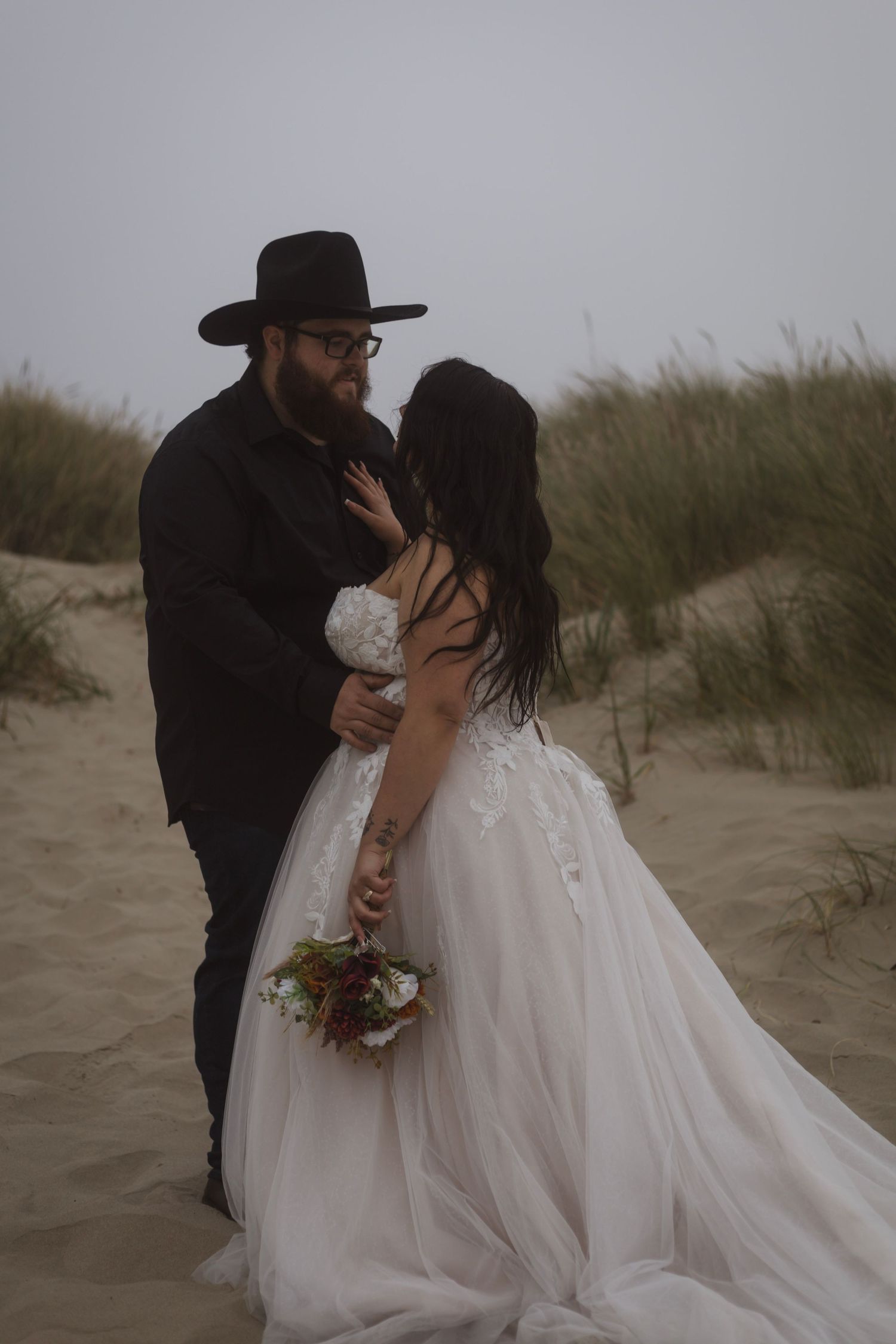 Romantic beach wedding photoshoot with flowing white dress against moody sand dunes.