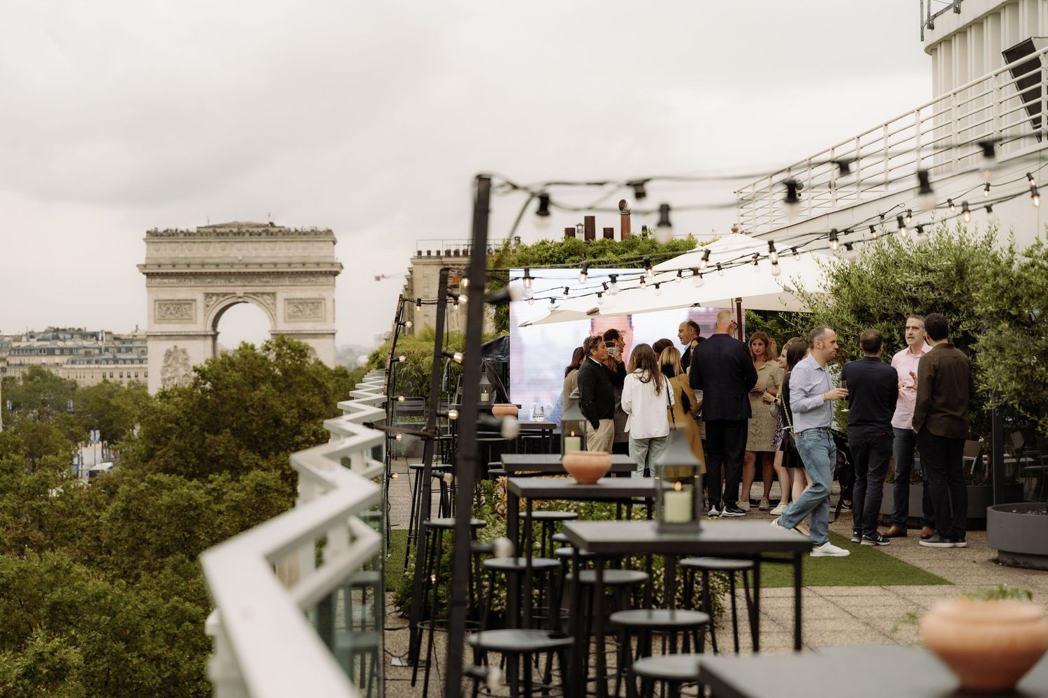 Guests enjoying an evening on the rooftop of a building overlooking the Arc de Triomphe in Paris