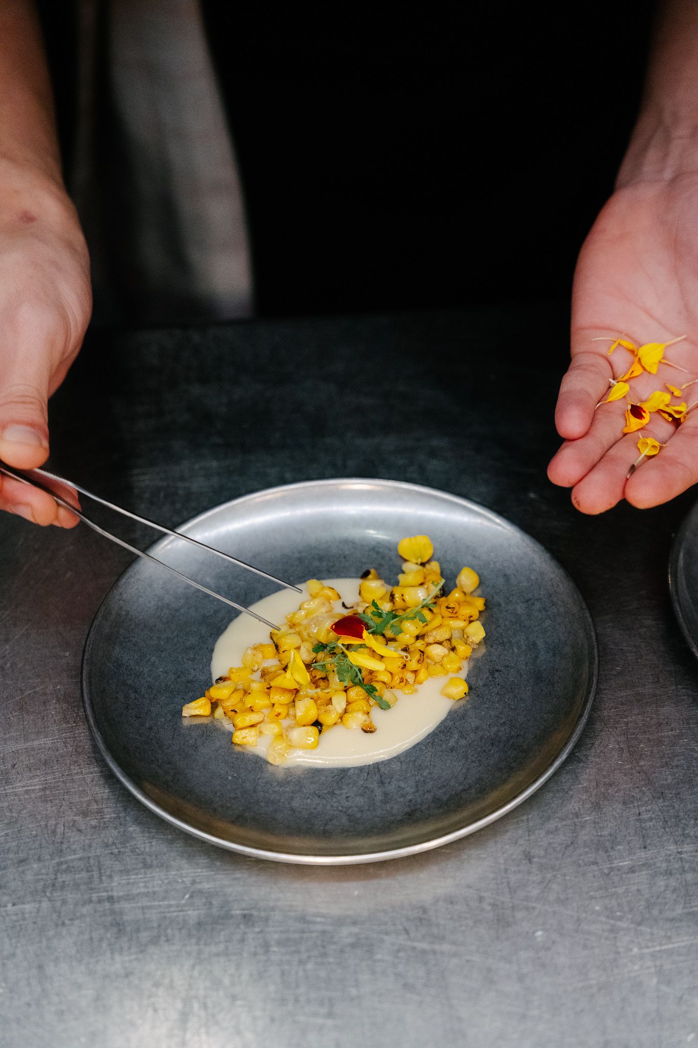 A cook plating his dish made of corn and sauce