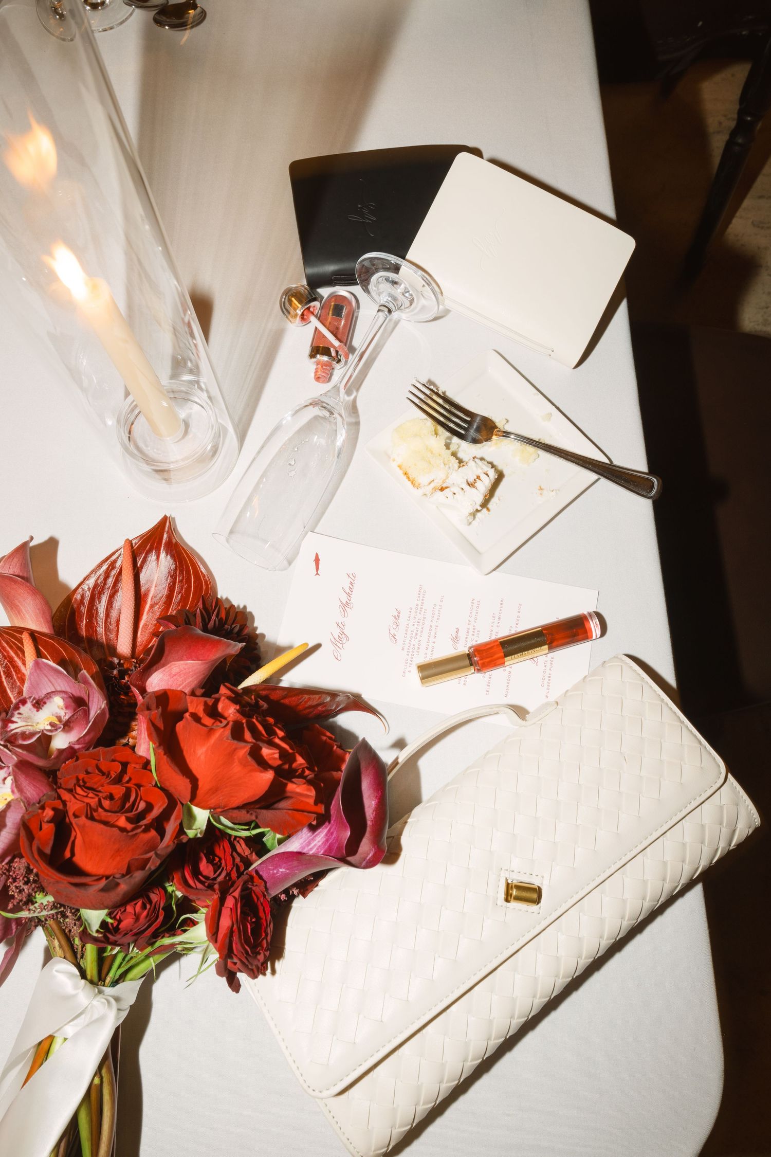 Red roses and table settings arranged on a white tablecloth at a wedding reception.