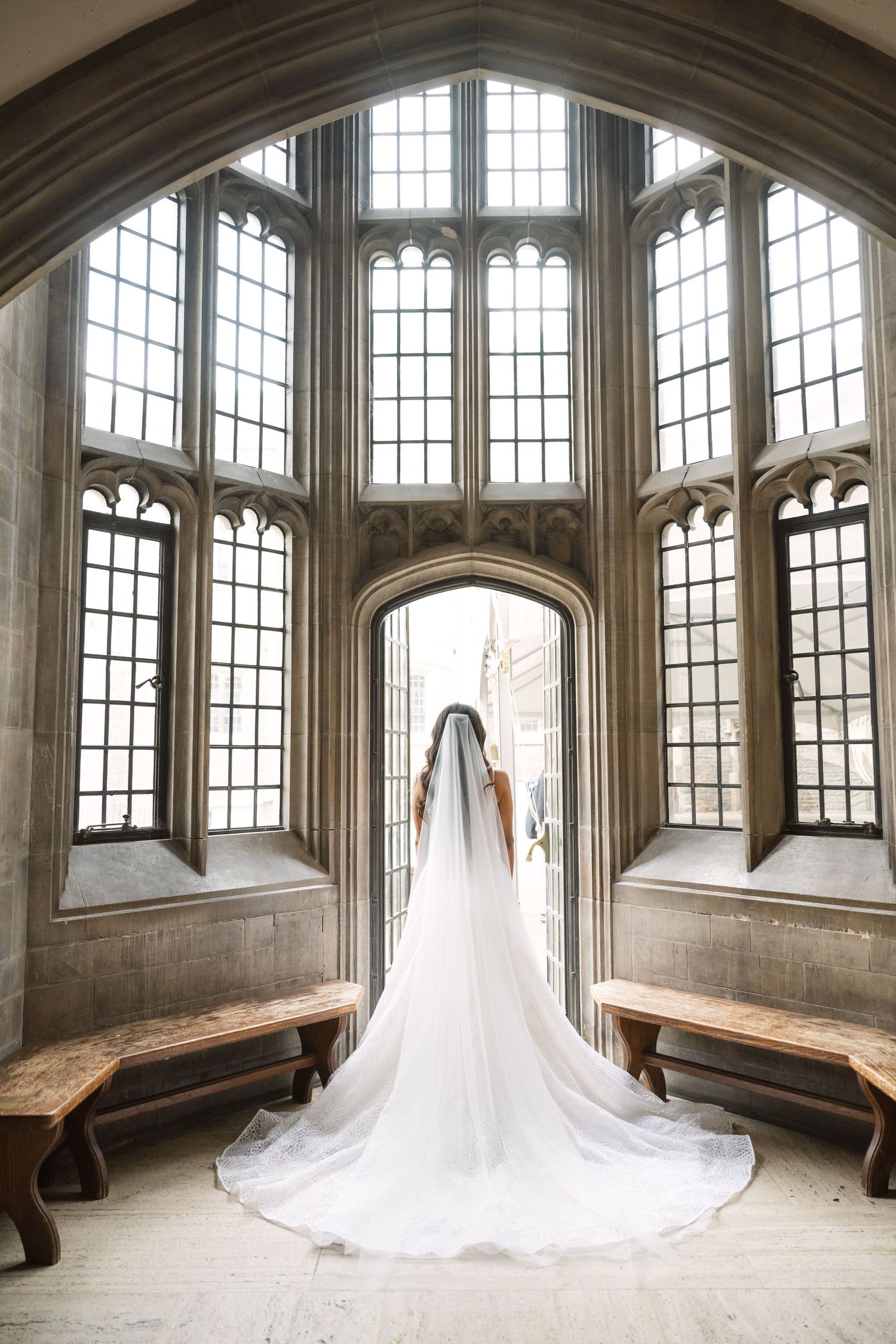 Dramatic bridal portrait in a gothic hall with soaring windows and a cathedral-length veil.