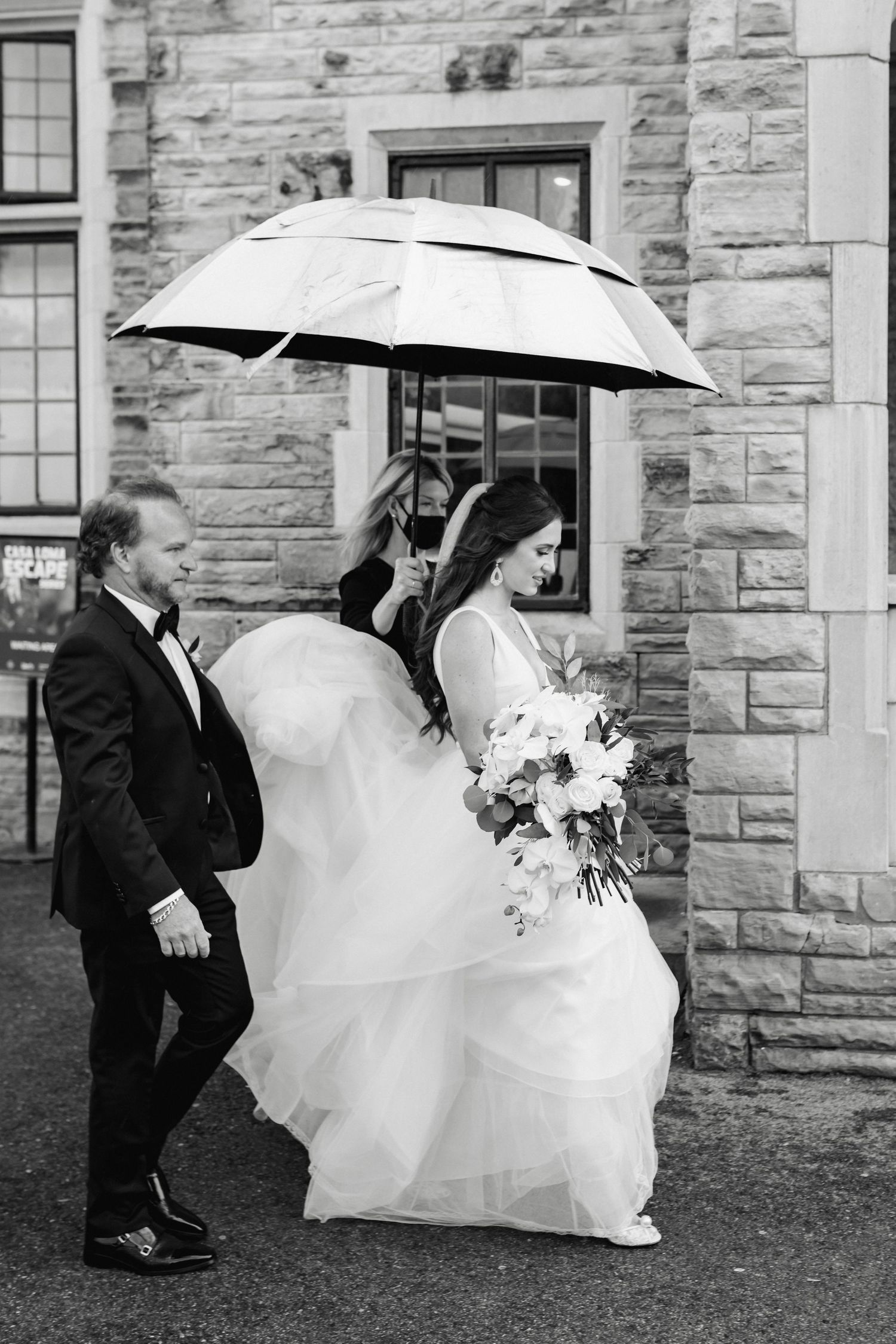 Bride being walked to her ceremony on a rainy day at Casa Loma, captured by a Toronto wedding photographer.