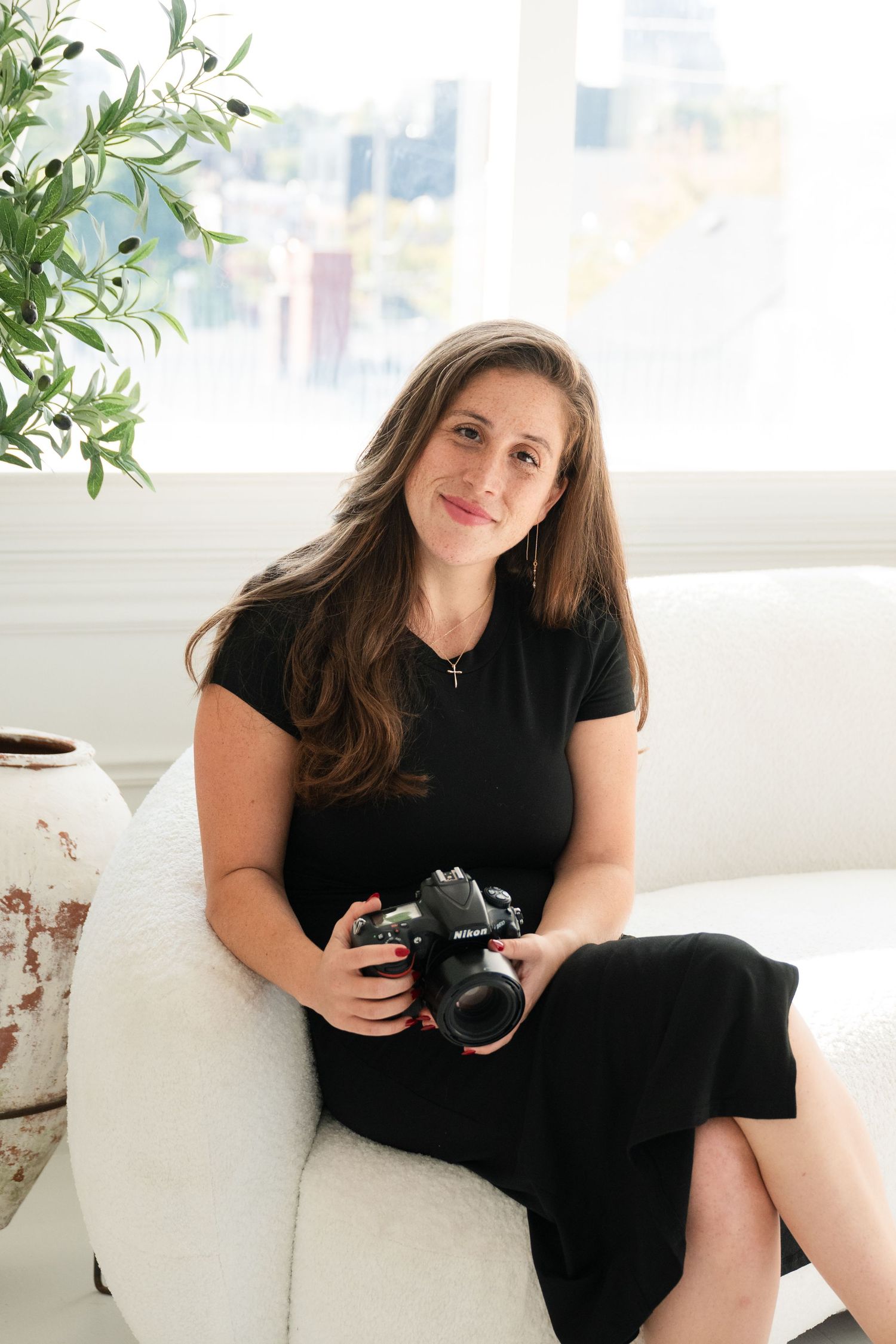 Portrait session featuring photographer with camera lounging on white couch by window.