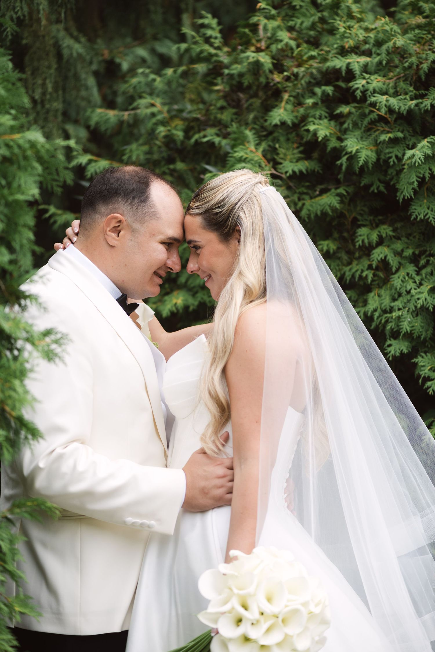 A romantic wedding moment captured in a garden setting with a flowing white veil and bouquet.