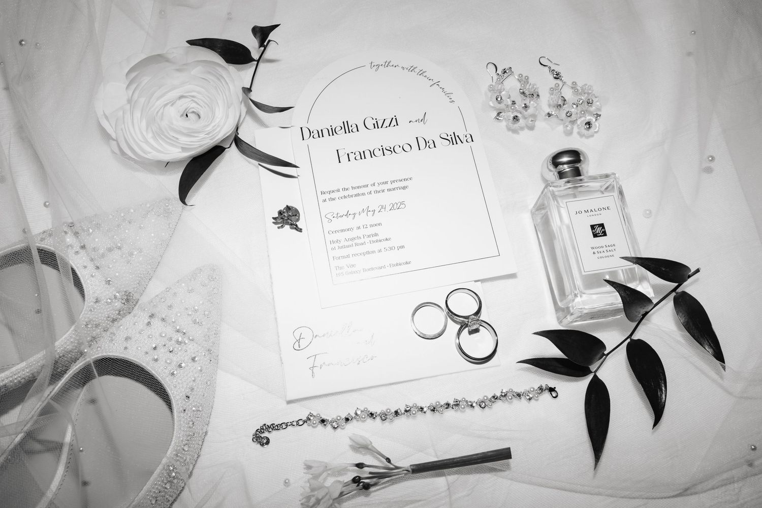 Black-and-white flat lay of wedding details of invitation, shoes, rings, and jewelry, shot with flash by a Toronto wedding photographer