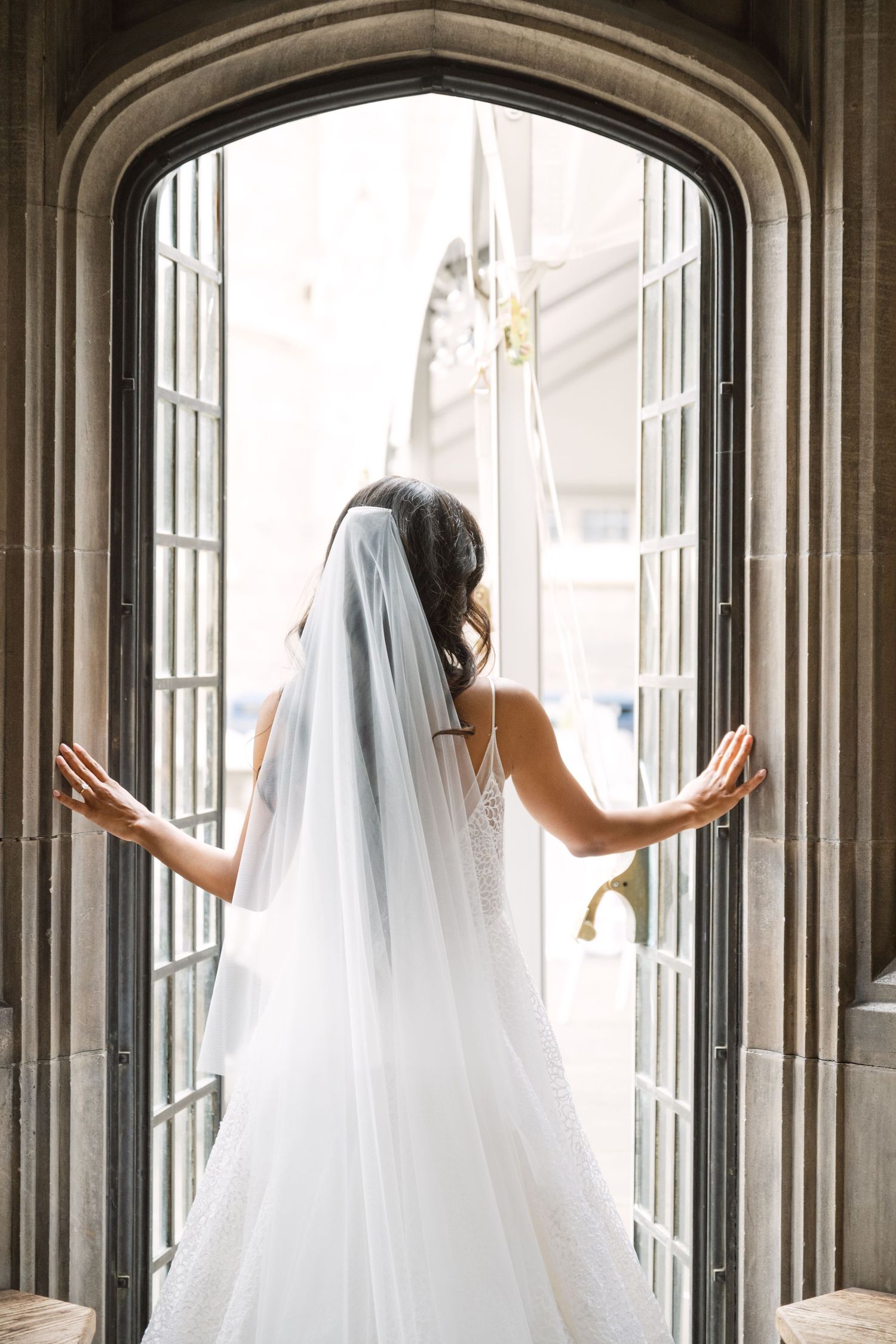 Bride in flowing veil poses elegantly in gothic stone archways.