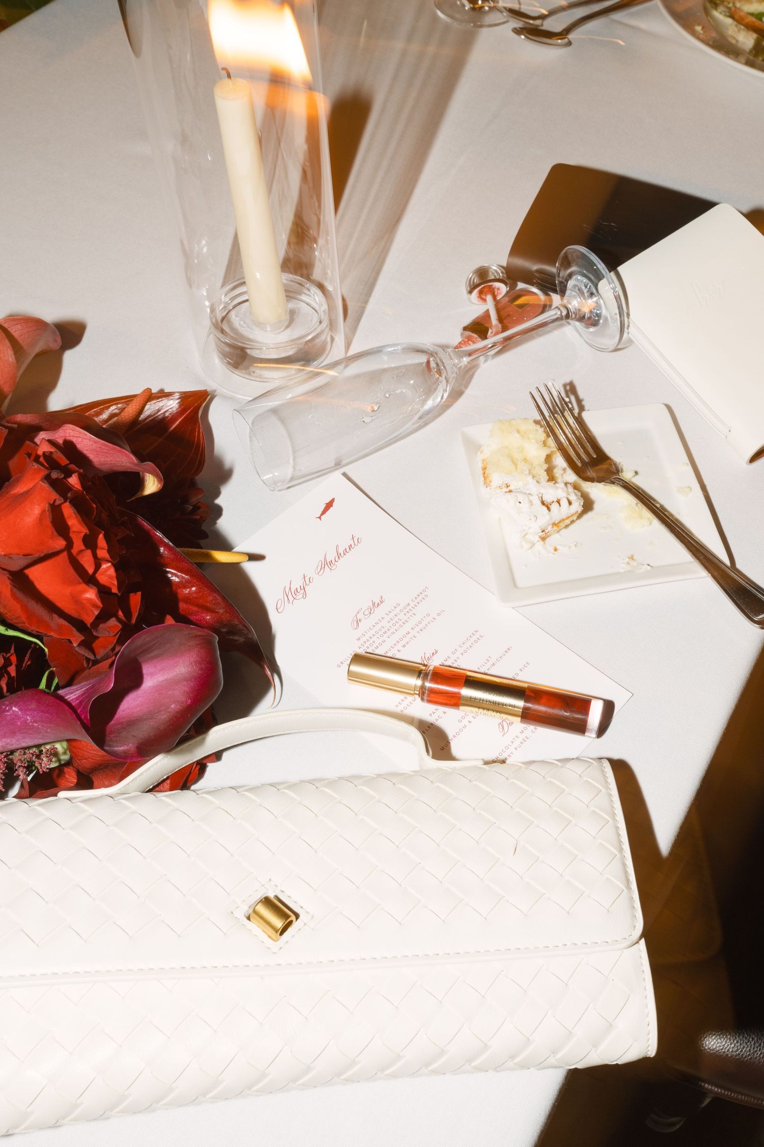 Wedding reception table details with white linens and scattered red rose petals.