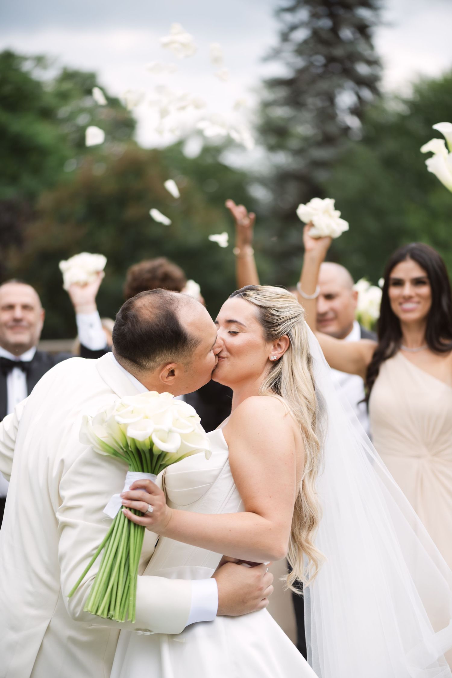 Wedding celebration with guests throwing white petals as the couple shares a kiss.