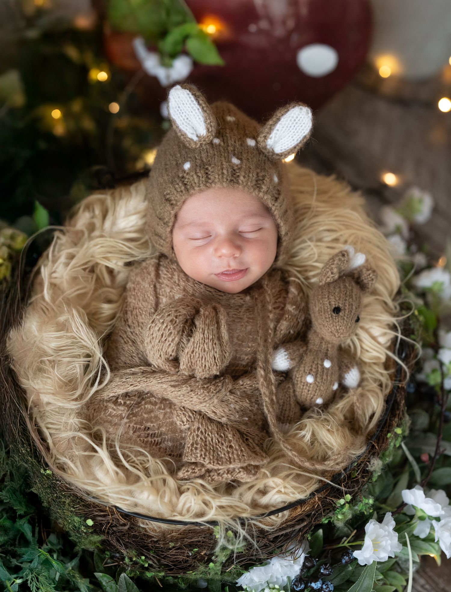 Sleeping newborn in brown knit deer outfit and bunny ear hat, nestled in a rustic nest with a matching stuffed animal.