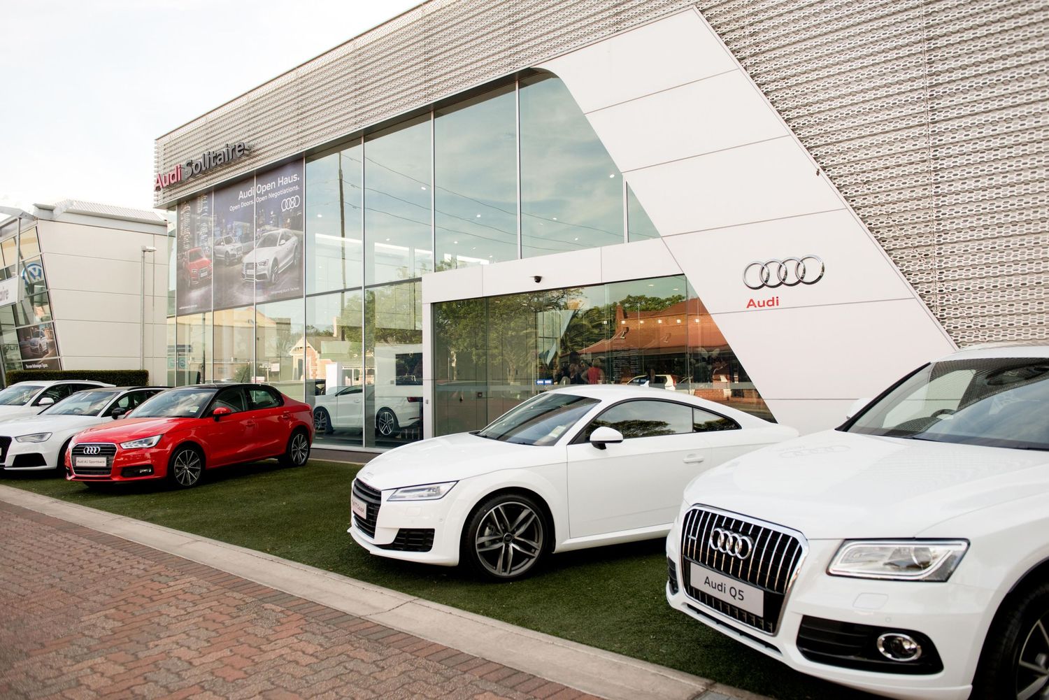 Row of white and red Audi luxury vehicles displayed at a modern car dealership showroom exterior. Commercial Photography.