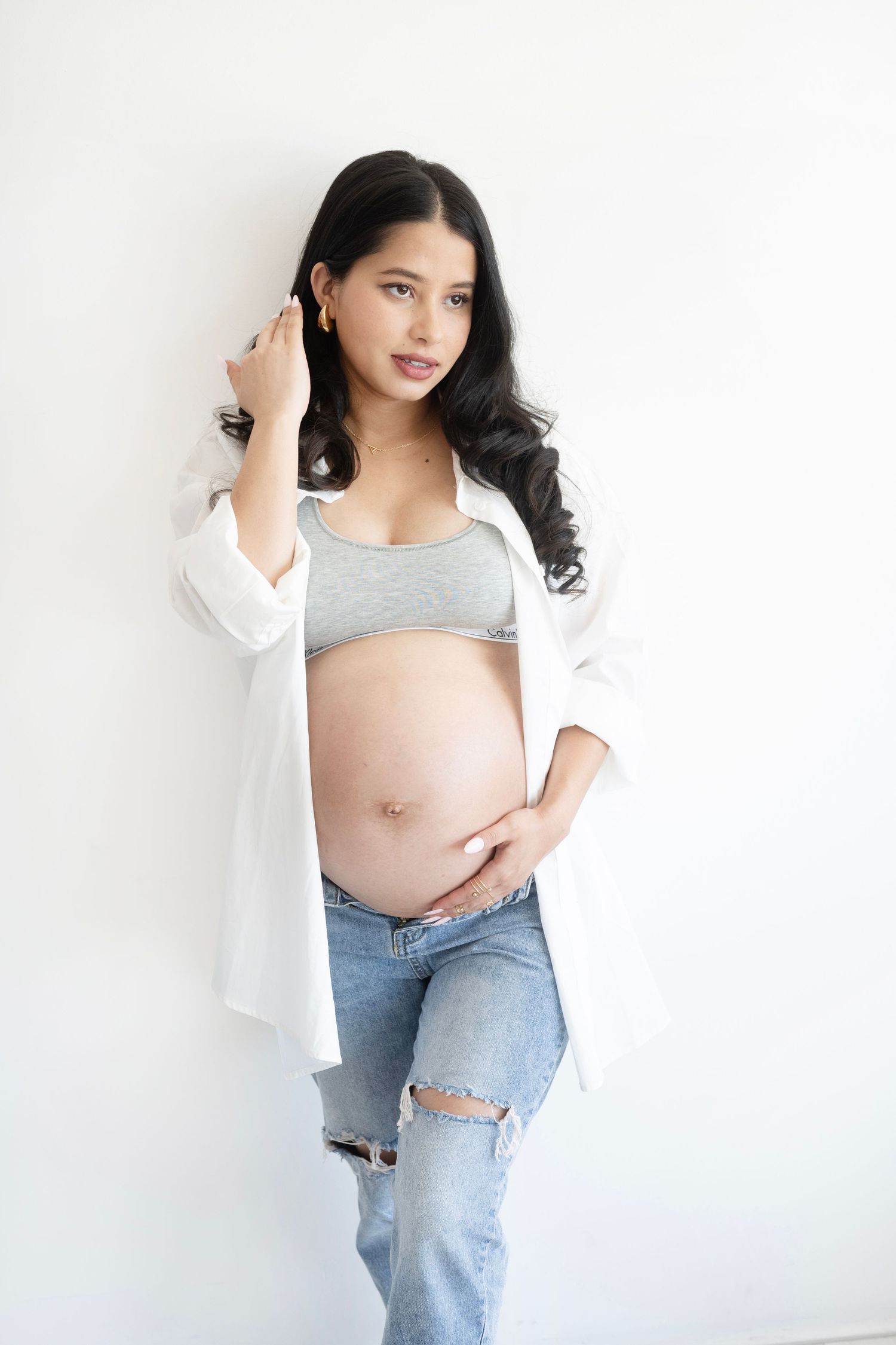 Maternity photo series showing a woman in ripped jeans and white top against a light background.