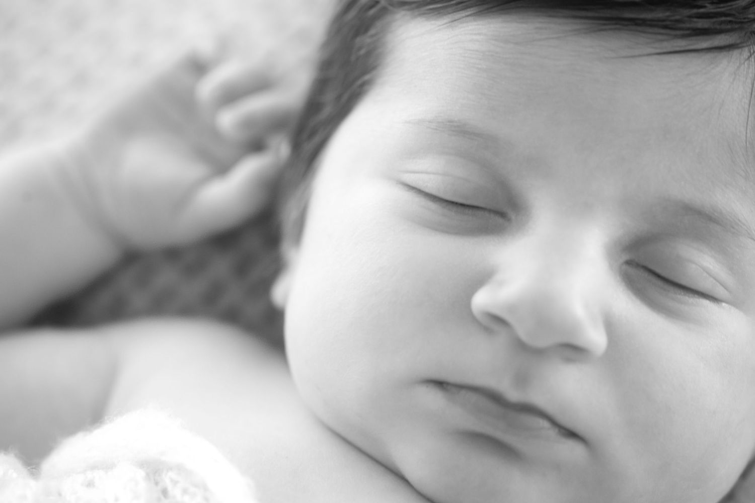 Black and white close-up photo of a peaceful sleeping newborn baby with dark hair and delicate features.