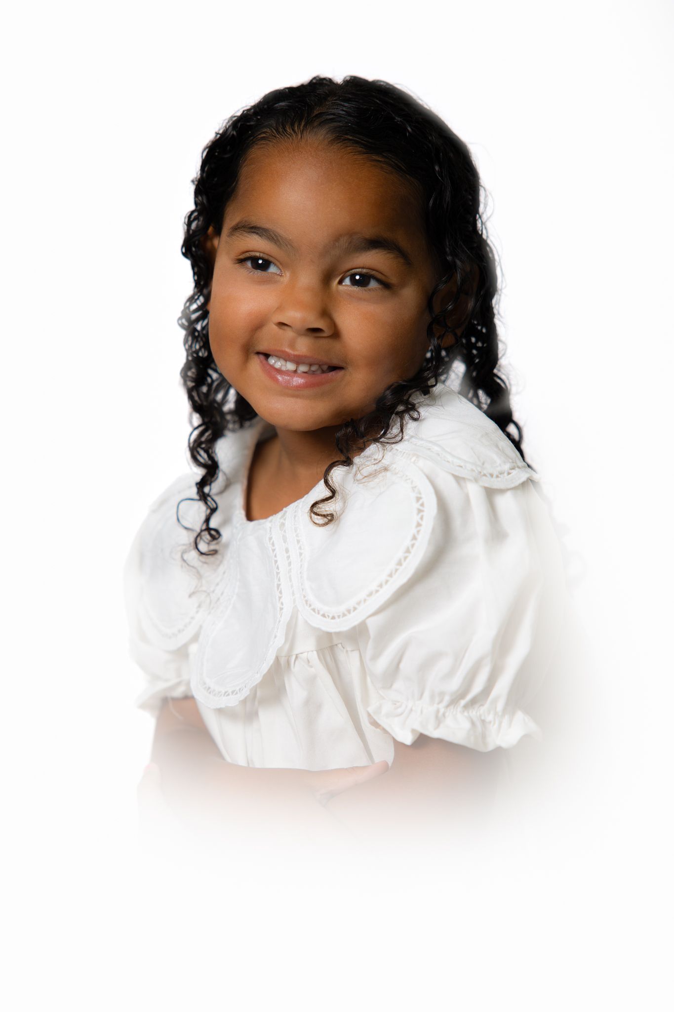 Adorable young African American girl smiling in white blouse with peter pan collar on white background.