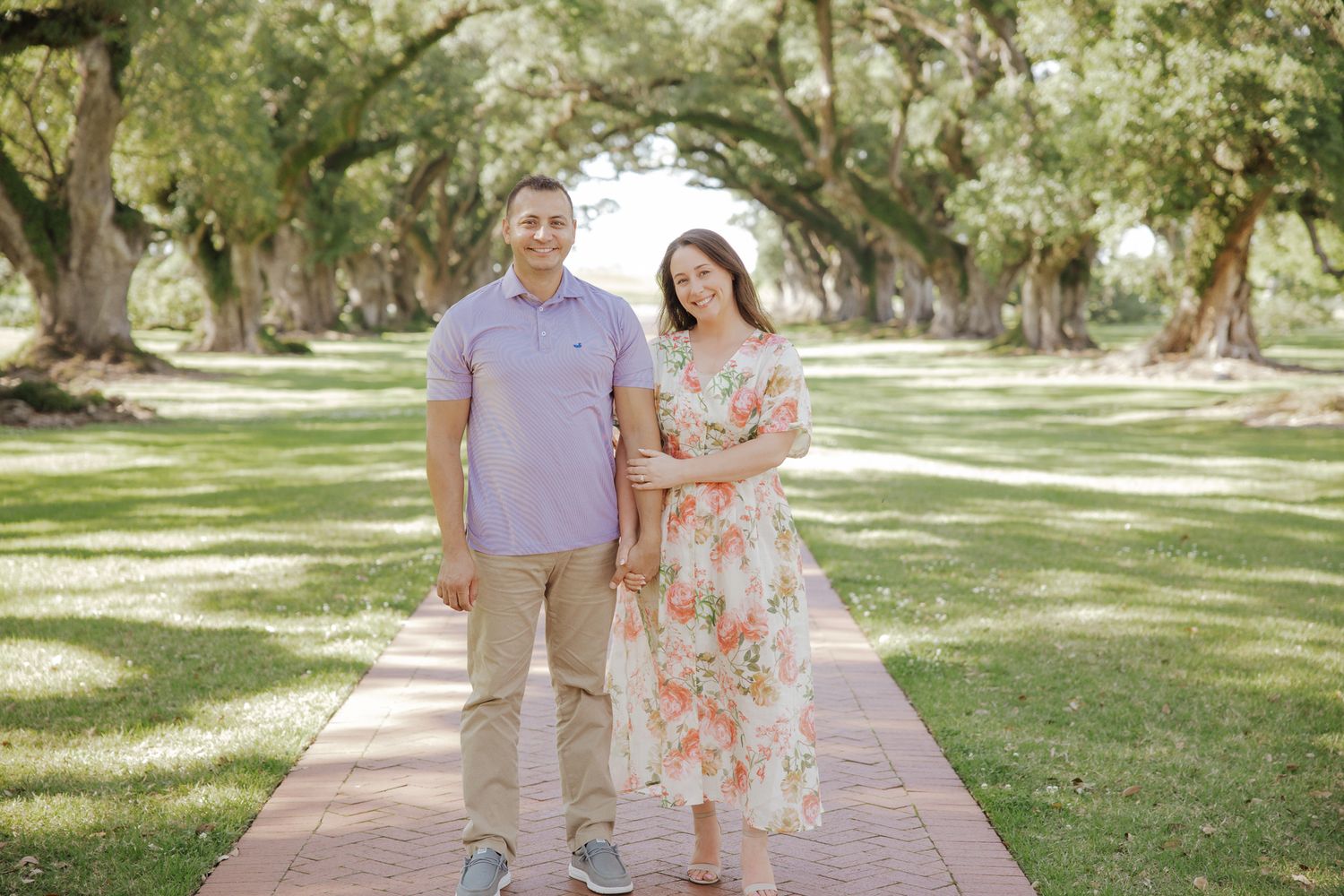Couple posing together on a brick walkway surrounded by large oak trees in a park.