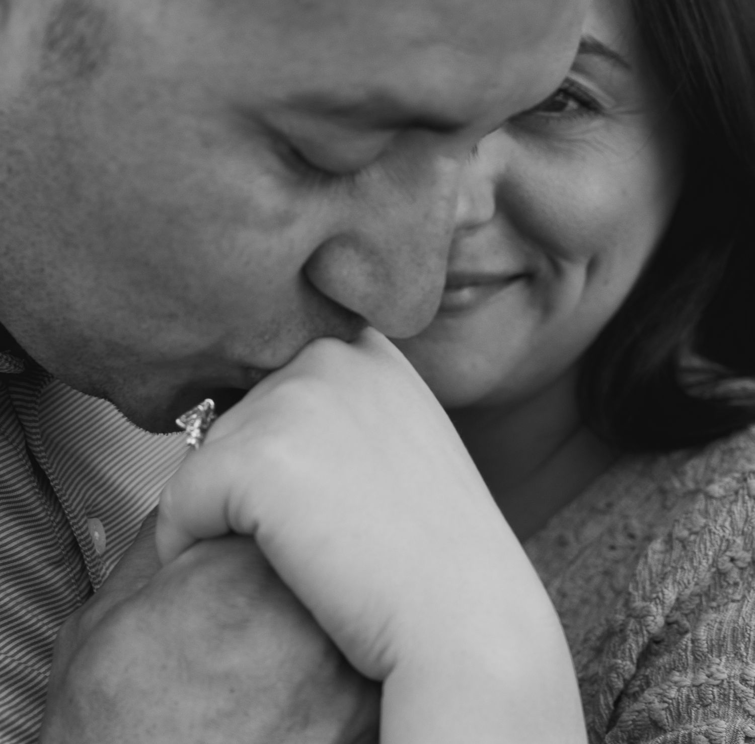 Black and white close-up of man kissing womans hand while she smiles warmly.