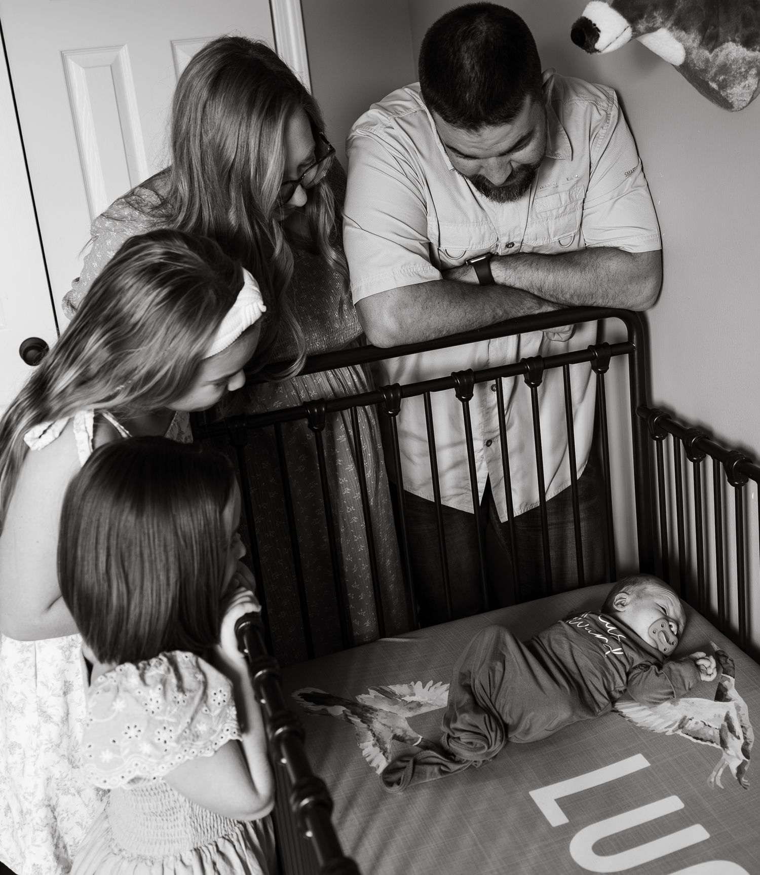 Black and white photo of family gathered around a crib admiring their newborn baby named Lucas.